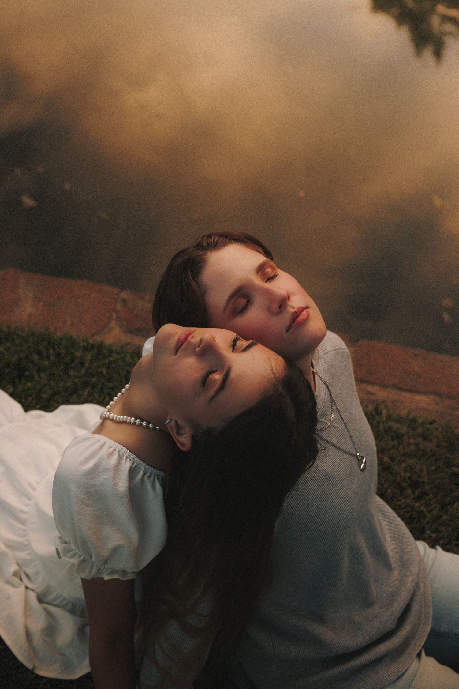 Two figures lying peacefully in the grass at dusk with dramatic moody lighting and soft natural tones.