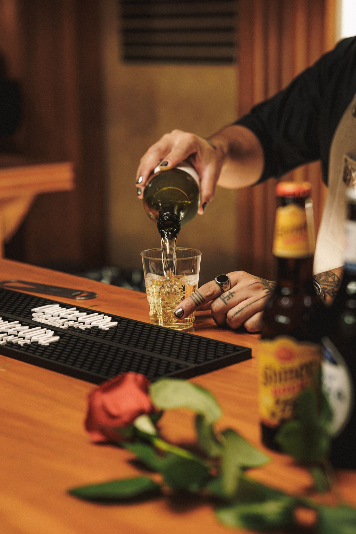 Tattooed bartender pouring beer into glass at wooden bar with a red rose in foreground.