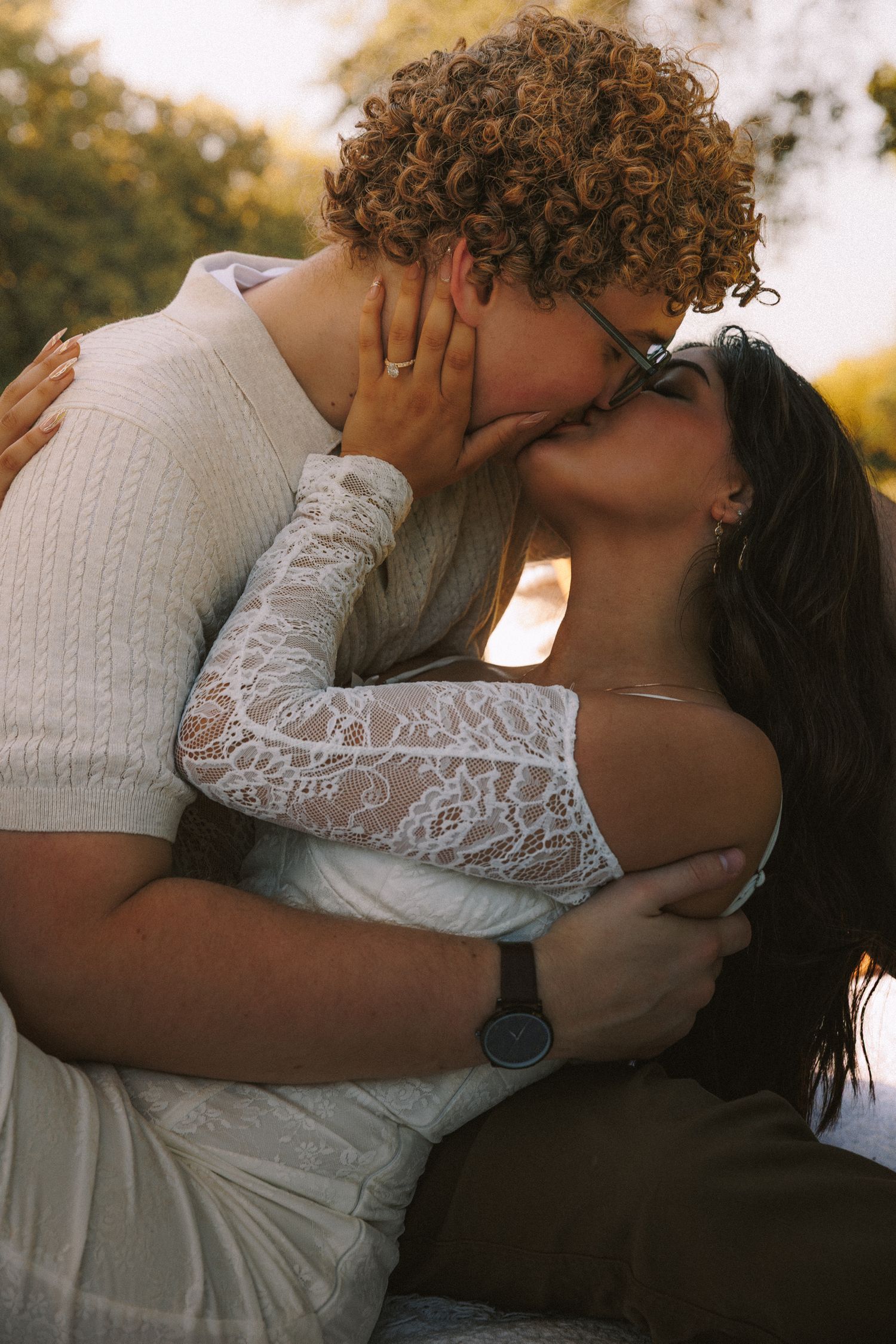 Intimate embrace captured in warm sunset lighting with white lace dress details.