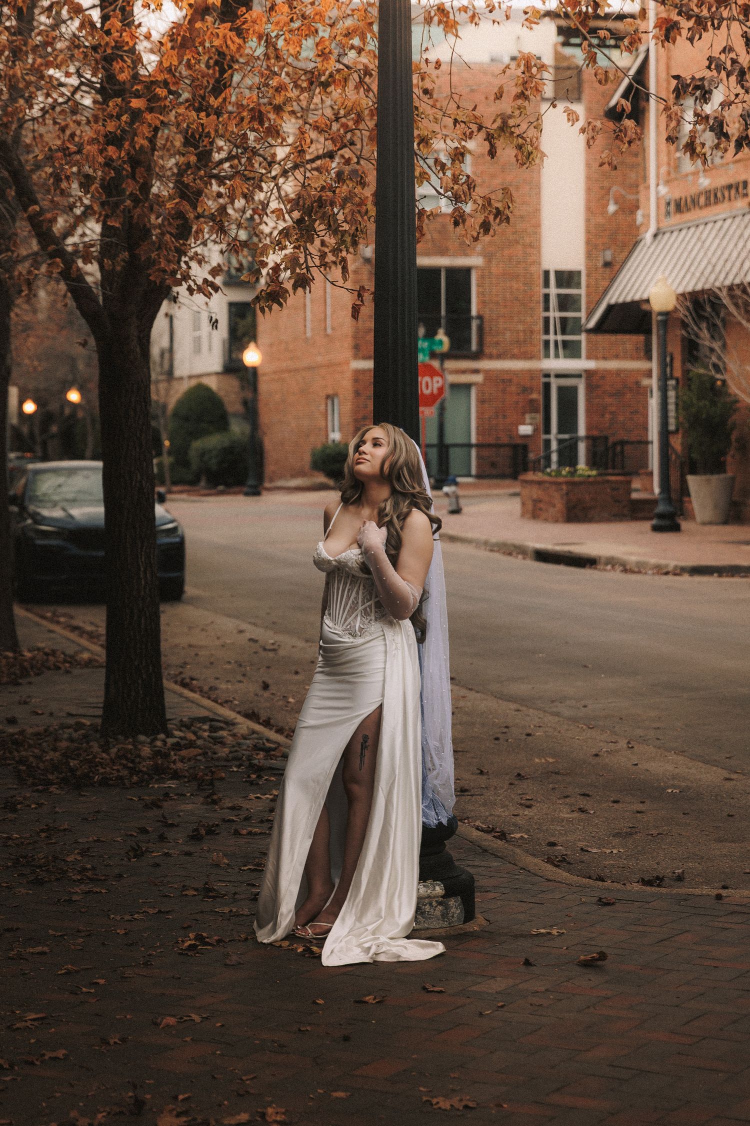 A figure in a flowing white dress dances gracefully among autumn trees on a brick-lined path at dusk.