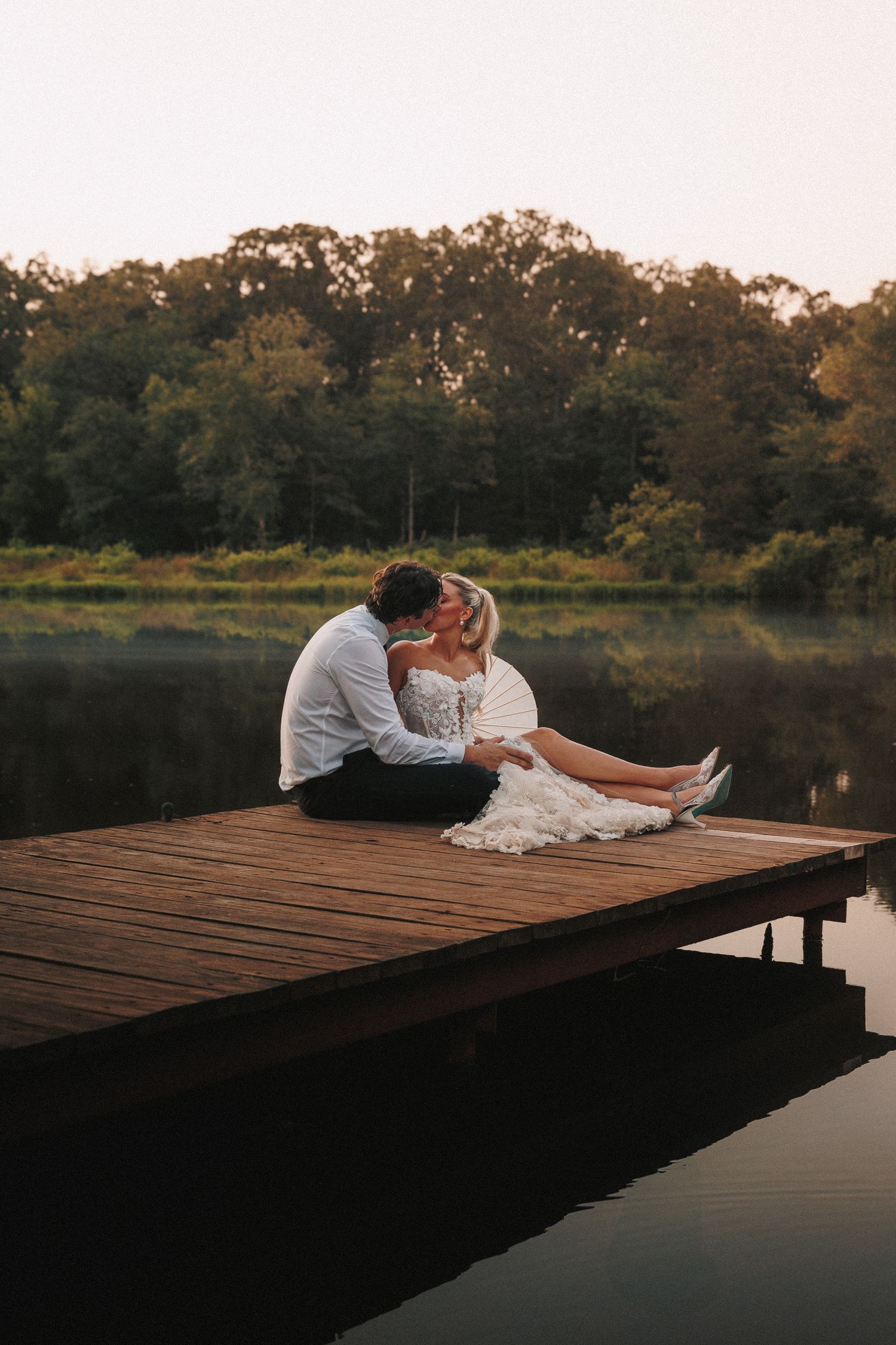 A couple sits intimately on a wooden dock over a tranquil lake during sunset.