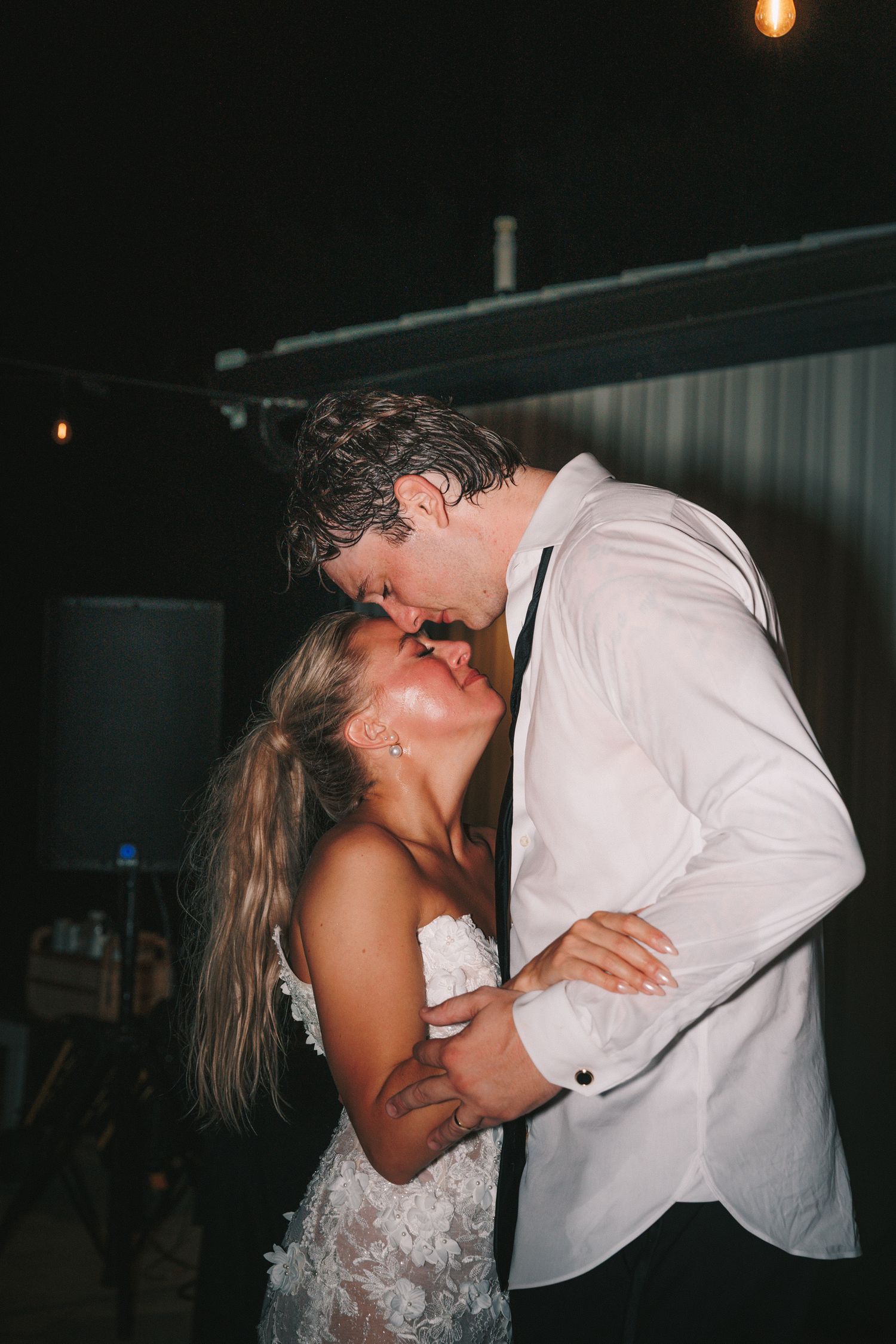 A couple shares an intimate dance moment under dim lighting at an evening event.
