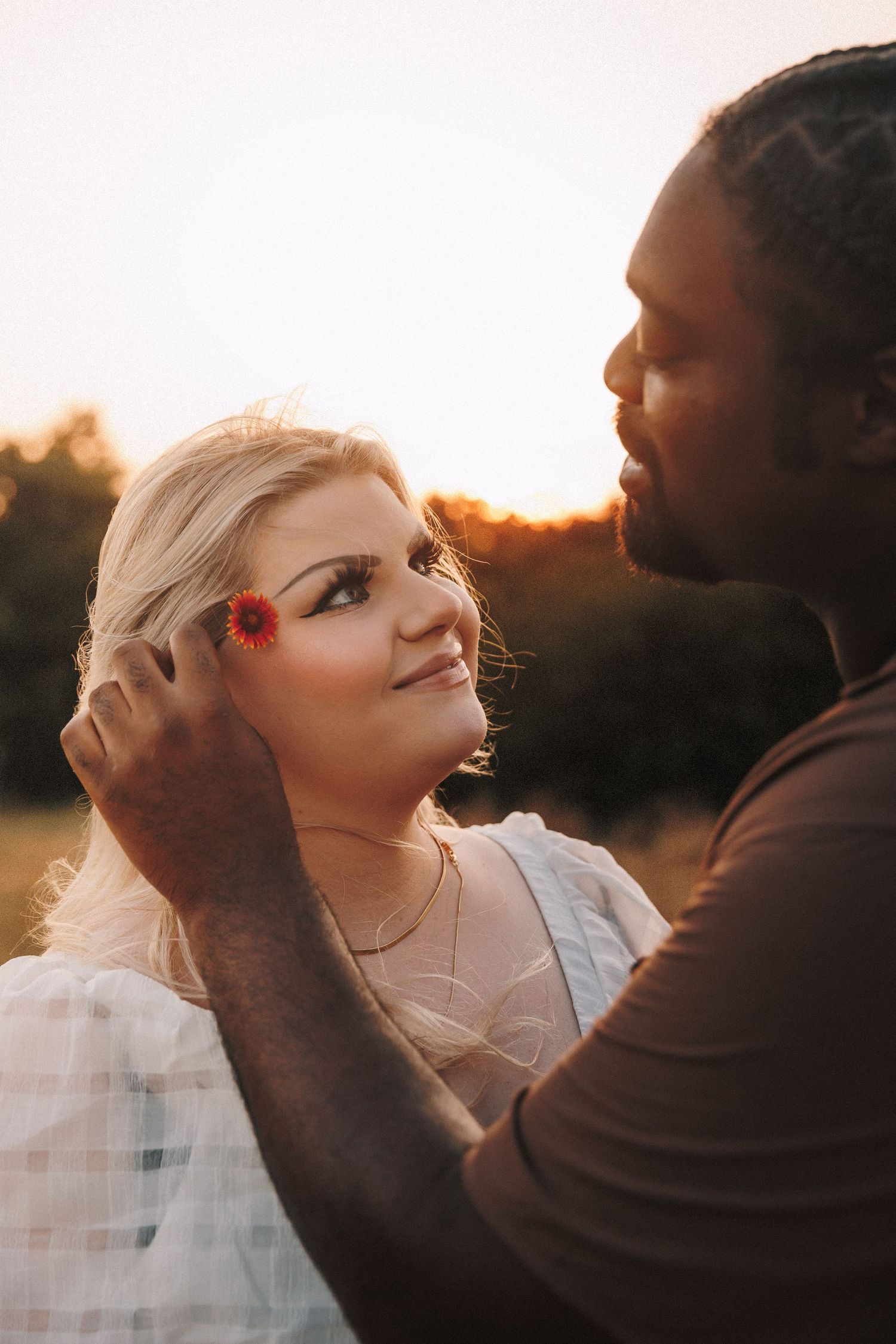 A romantic couple embraces during sunset in a dreamy outdoor setting with warm golden light filtering through the scene.
