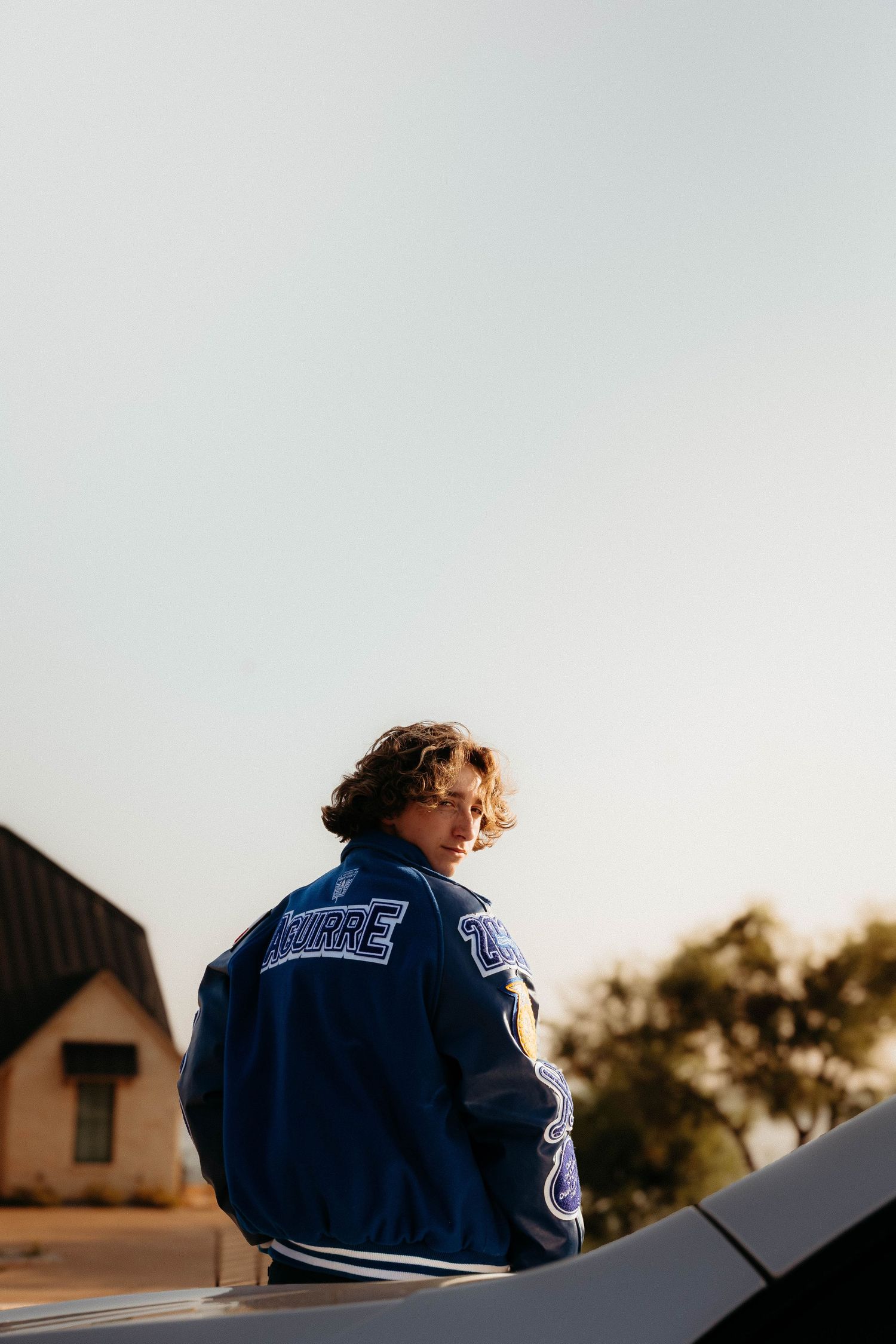 Back view of a person in a varsity jacket silhouetted against a light sky during sunset.