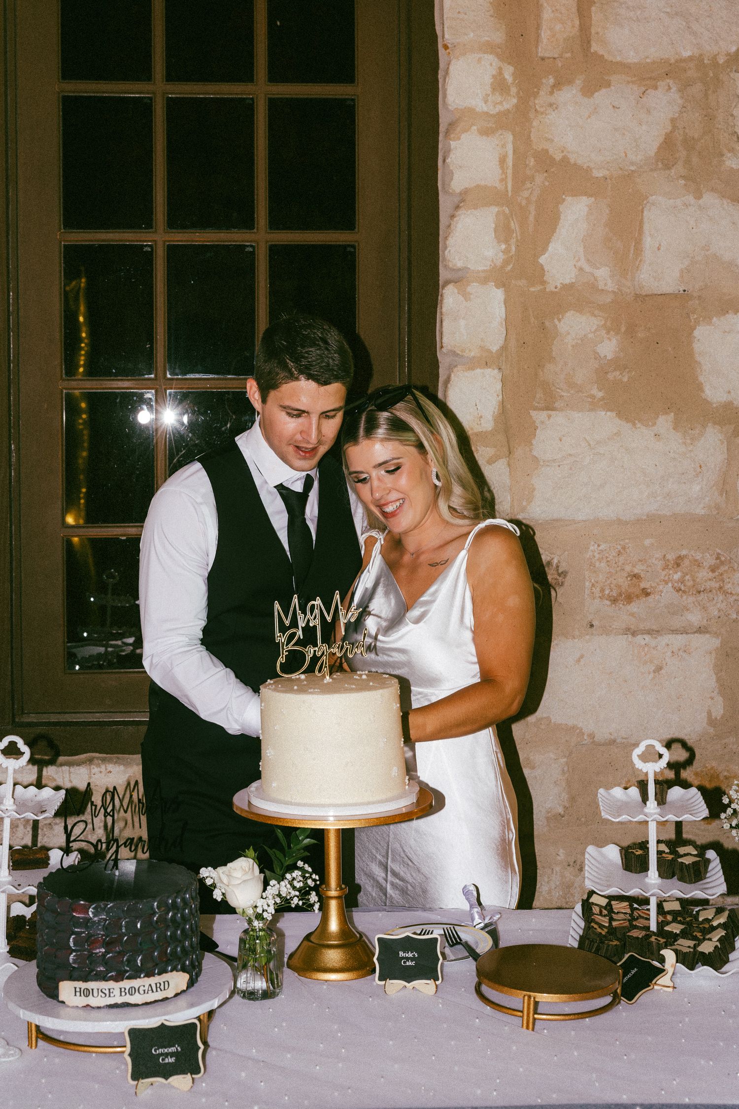Bride and groom cut their white wedding cake at a rustic stone venue reception table.