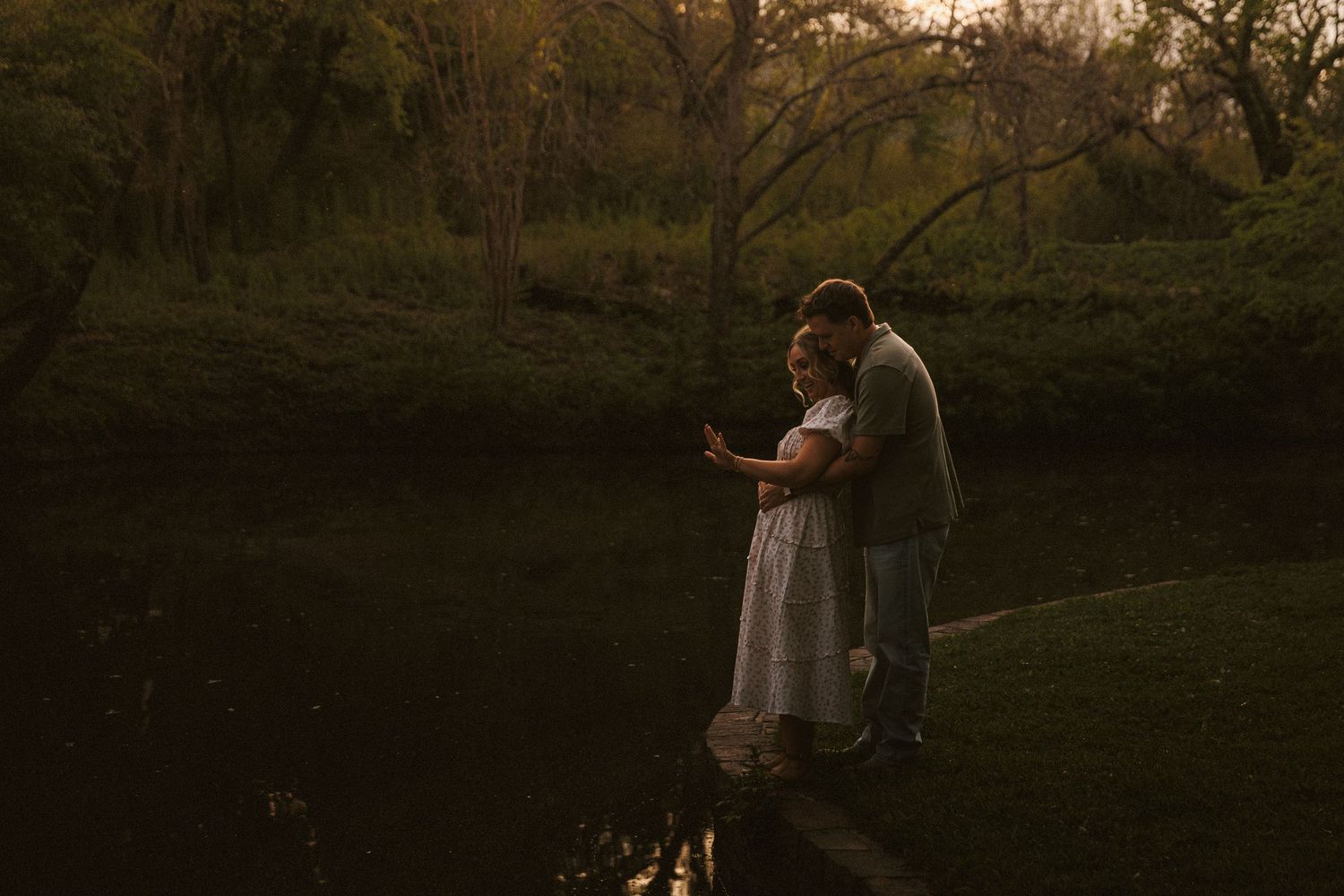 Couple standing together on a dock by a calm river in a wooded park.