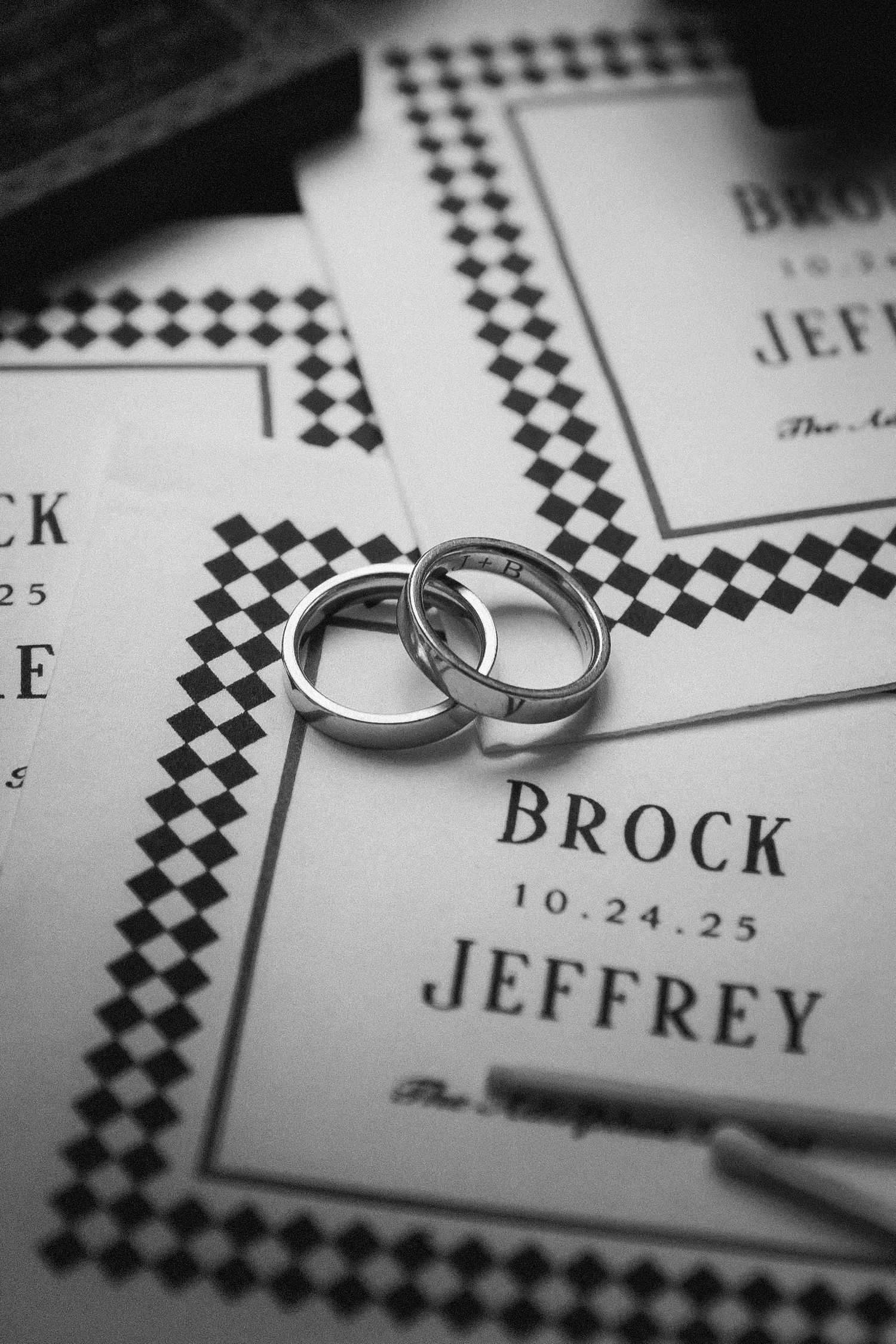 Two silver wedding bands resting on black and white houndstooth wedding invitations for Brock and Jeffrey.