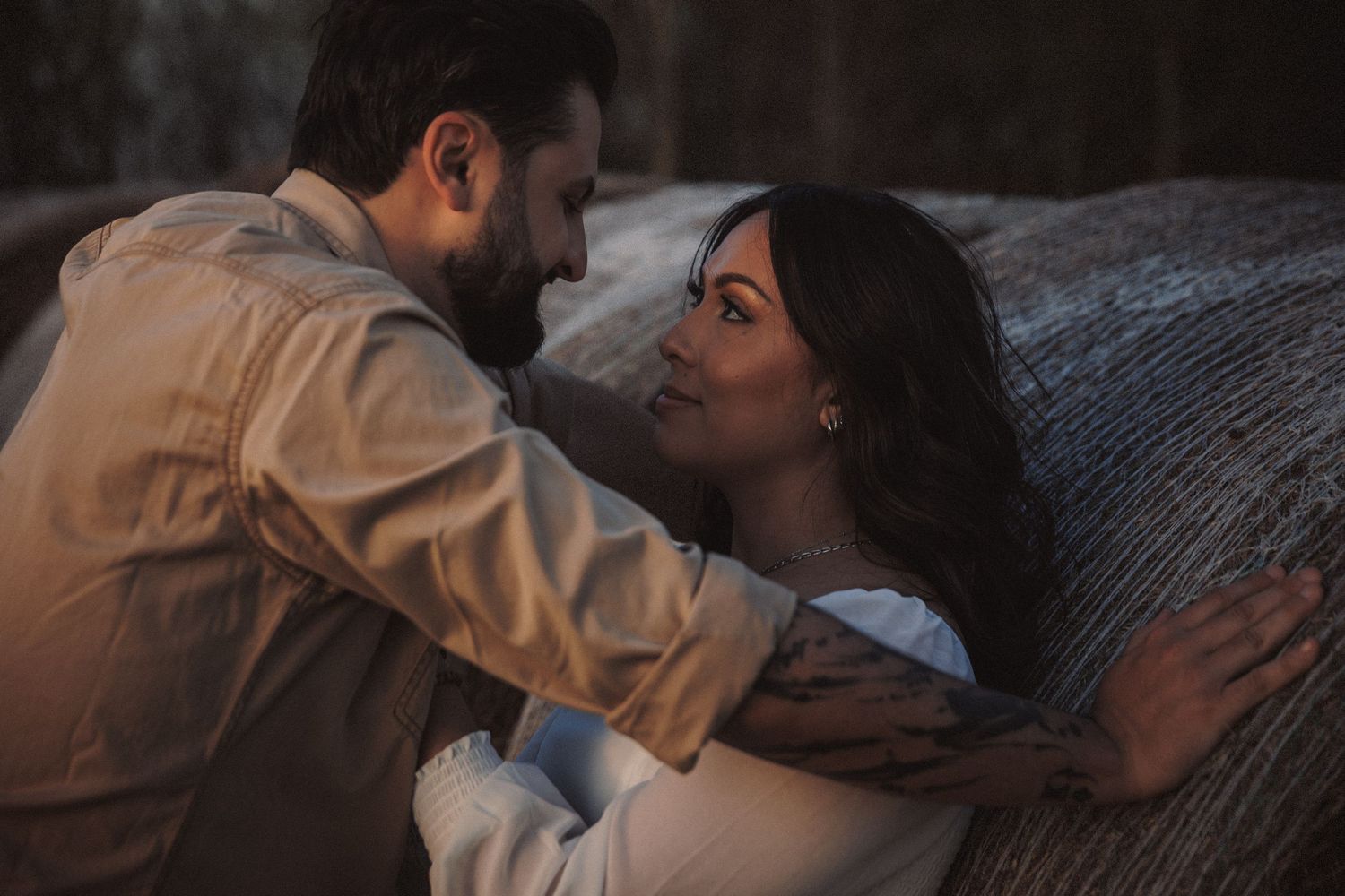 Romantic couple sharing an intimate moment, man in beige shirt embracing woman in white near a textured wall.
