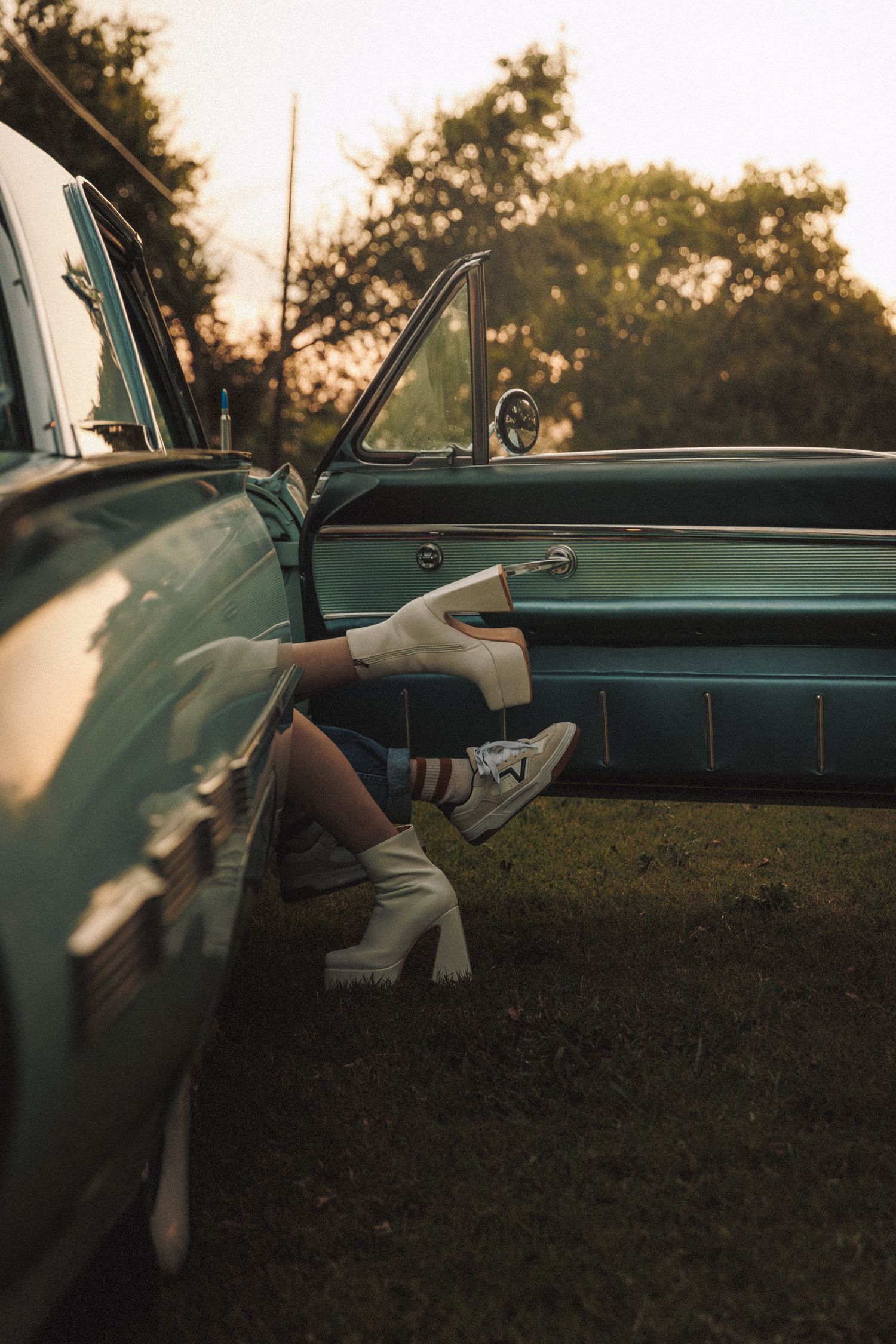 Legs with white sneakers dangle from vintage car door at sunset, showing turquoise interior upholstery.