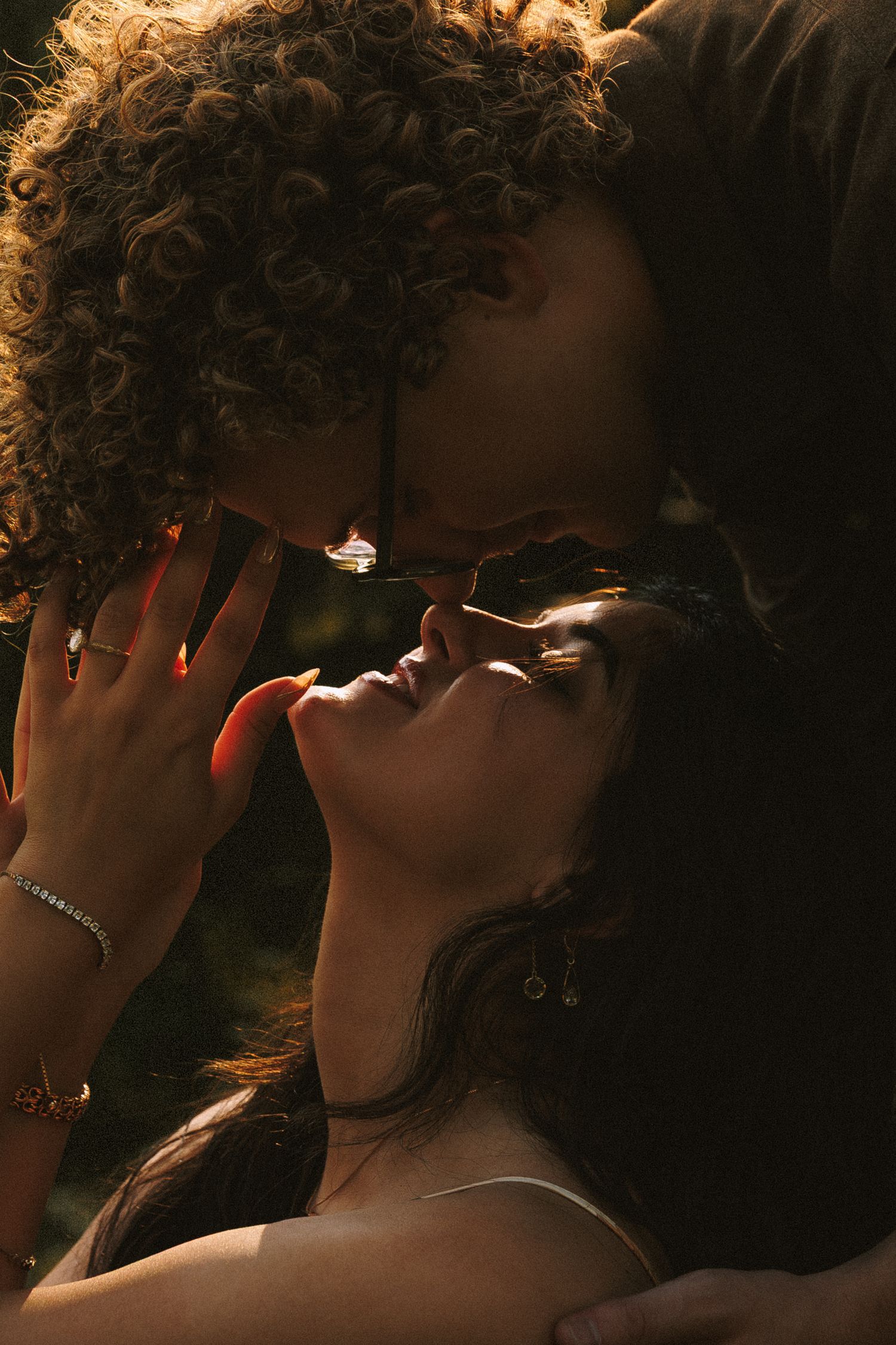 Intimate silhouette of two people sharing a tender moment in golden sunlight with curly hair and jewelry details.