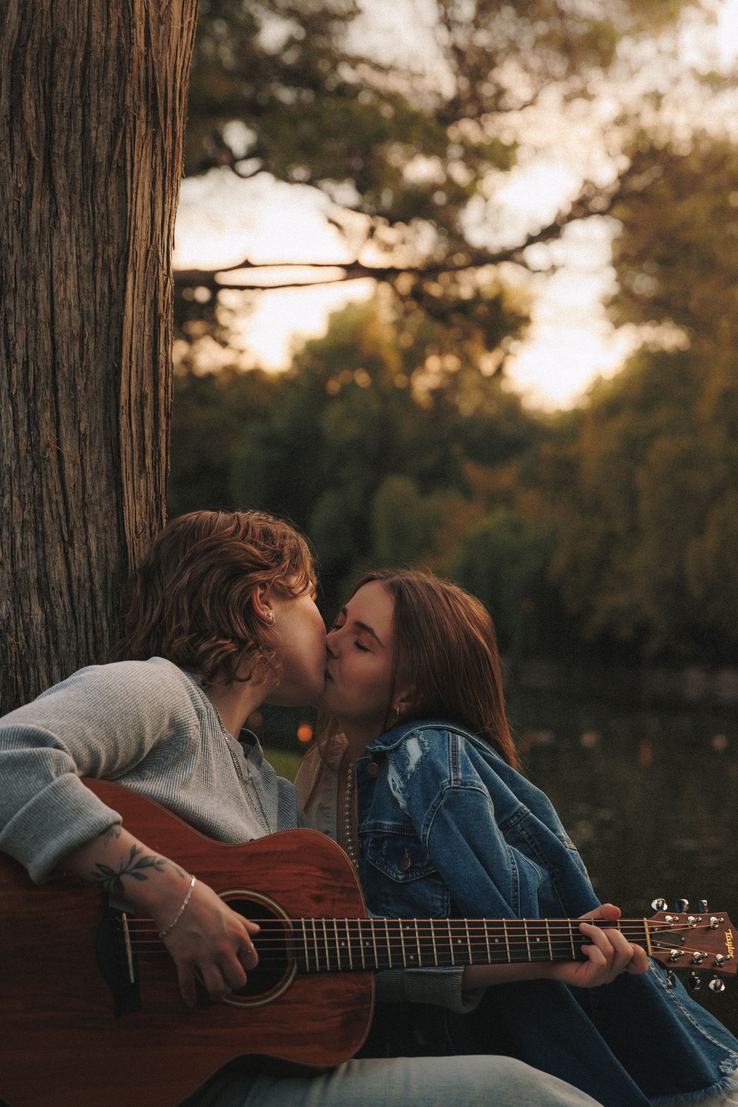 A couple shares a romantic moment while playing acoustic guitar together in a forest during golden hour sunset.
