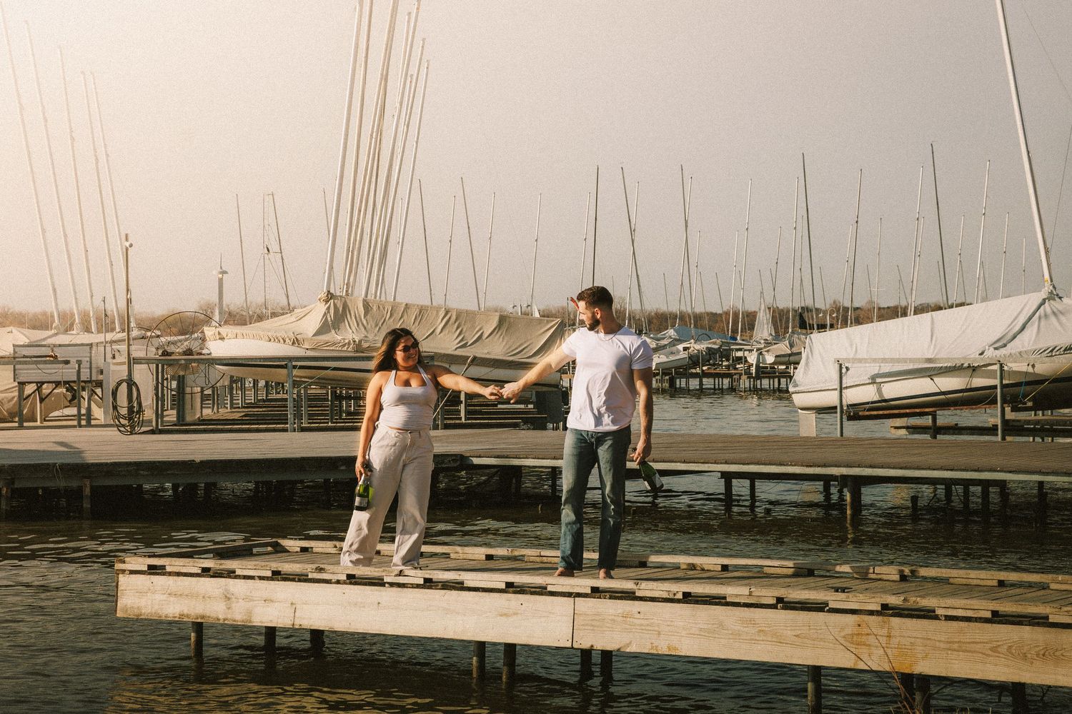 People walking along a wooden dock with sailboats moored in the marina during a sunny afternoon.