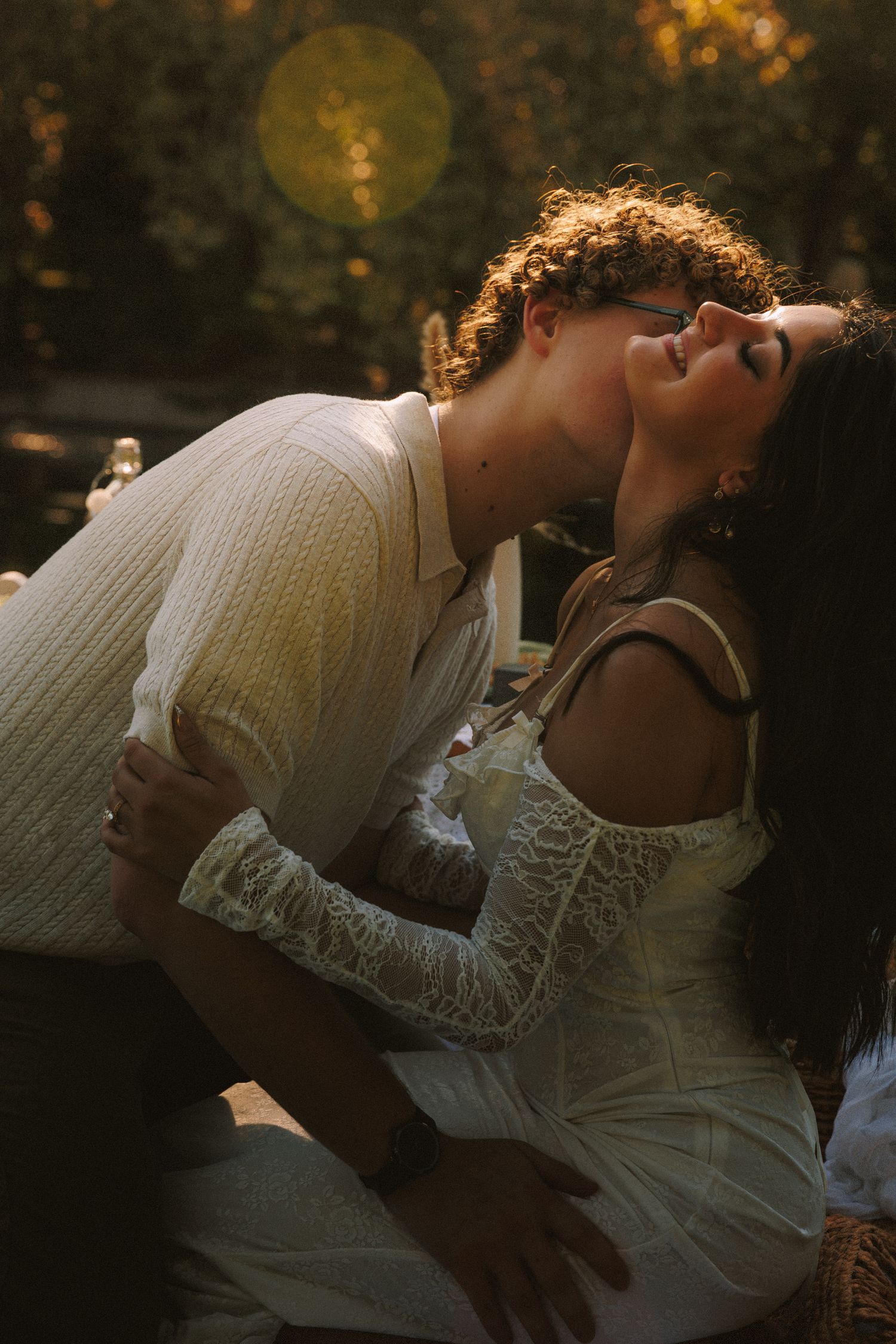 Romantic couple sharing intimate moment under warm sunlight in natural outdoor setting.