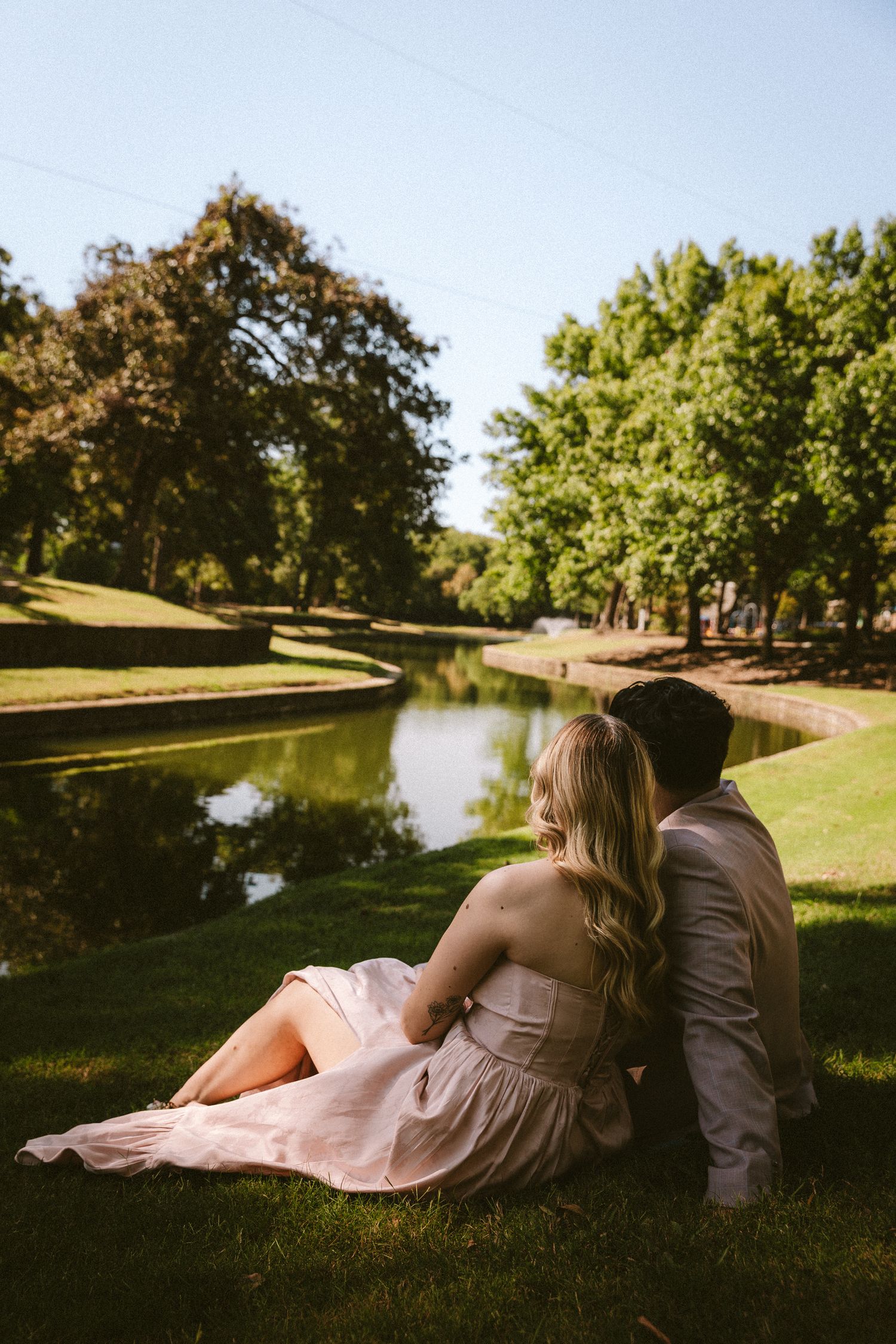 A couple relaxing by a pond in a park during a sunny afternoon.