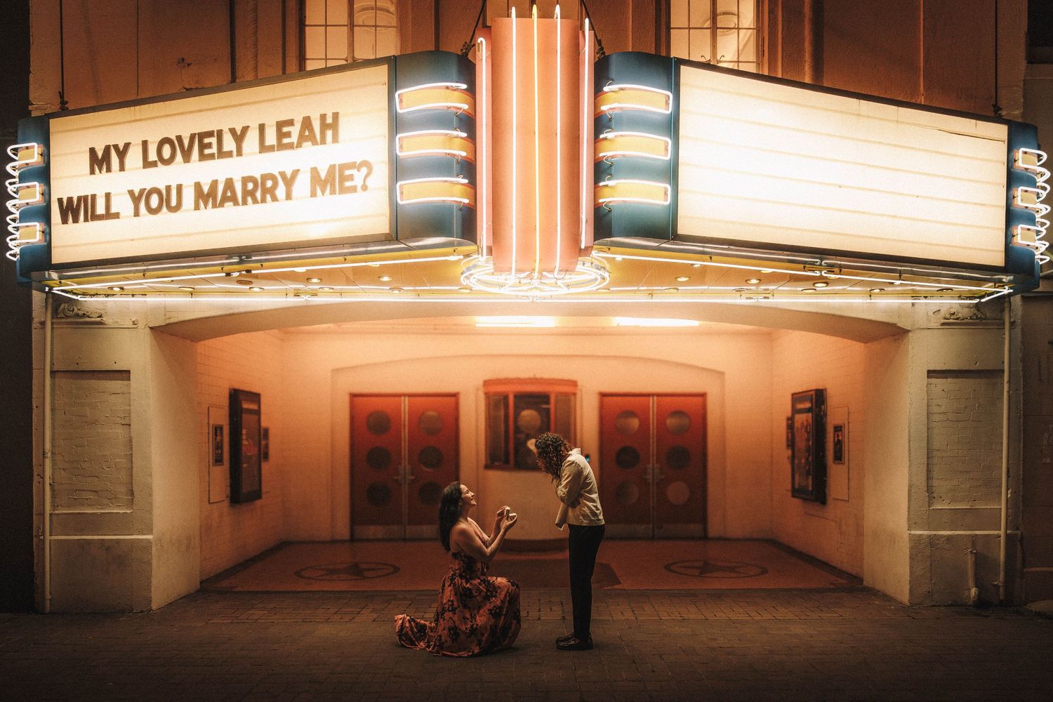 Illuminated movie theater marquee sign displaying 'MY LOVELY LEAH' and 'WILL YOU MARRY ME?' in bright lights at night.