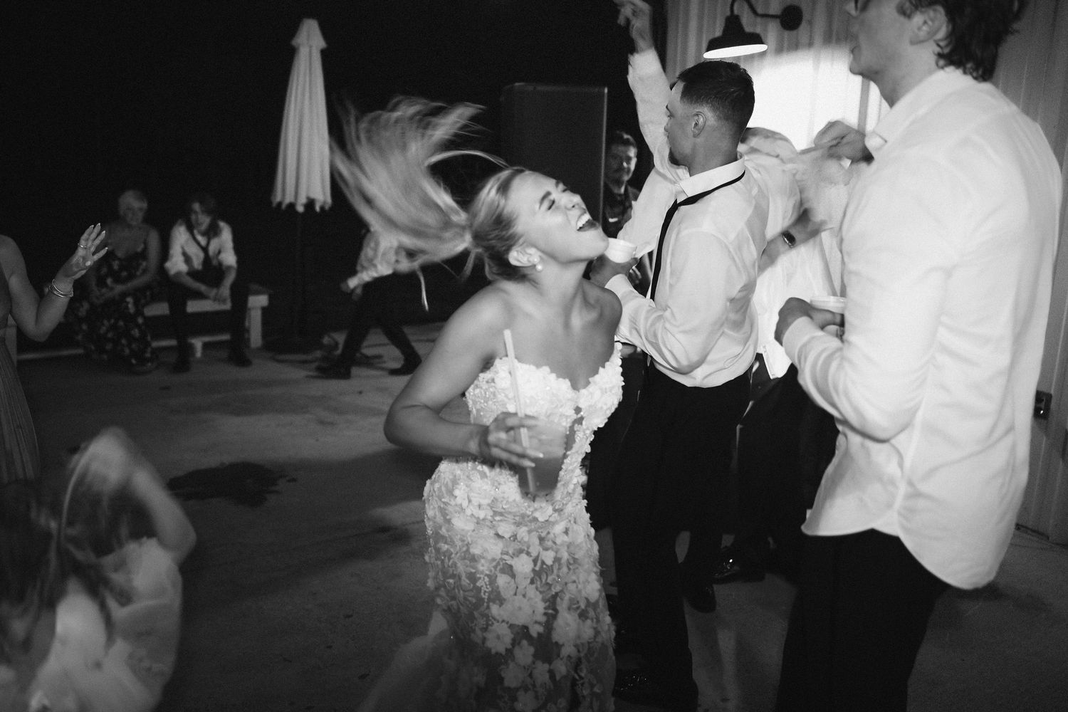 Black and white photo captures energetic dancing moment at outdoor wedding reception.