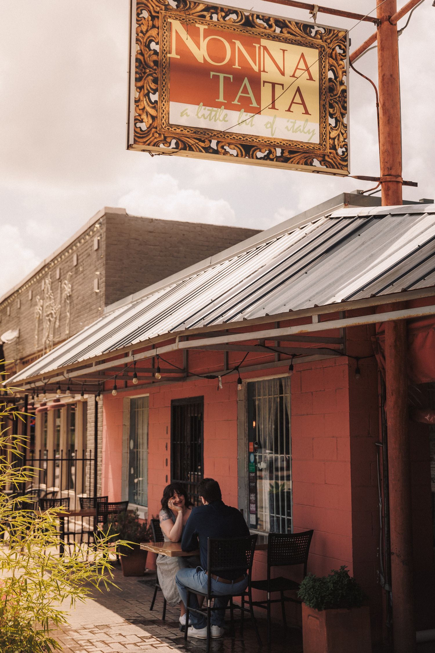 Sun-lit exterior of a rustic building with framed signs reading 'Nonna' and 'Tata' mounted on salmon-colored walls.