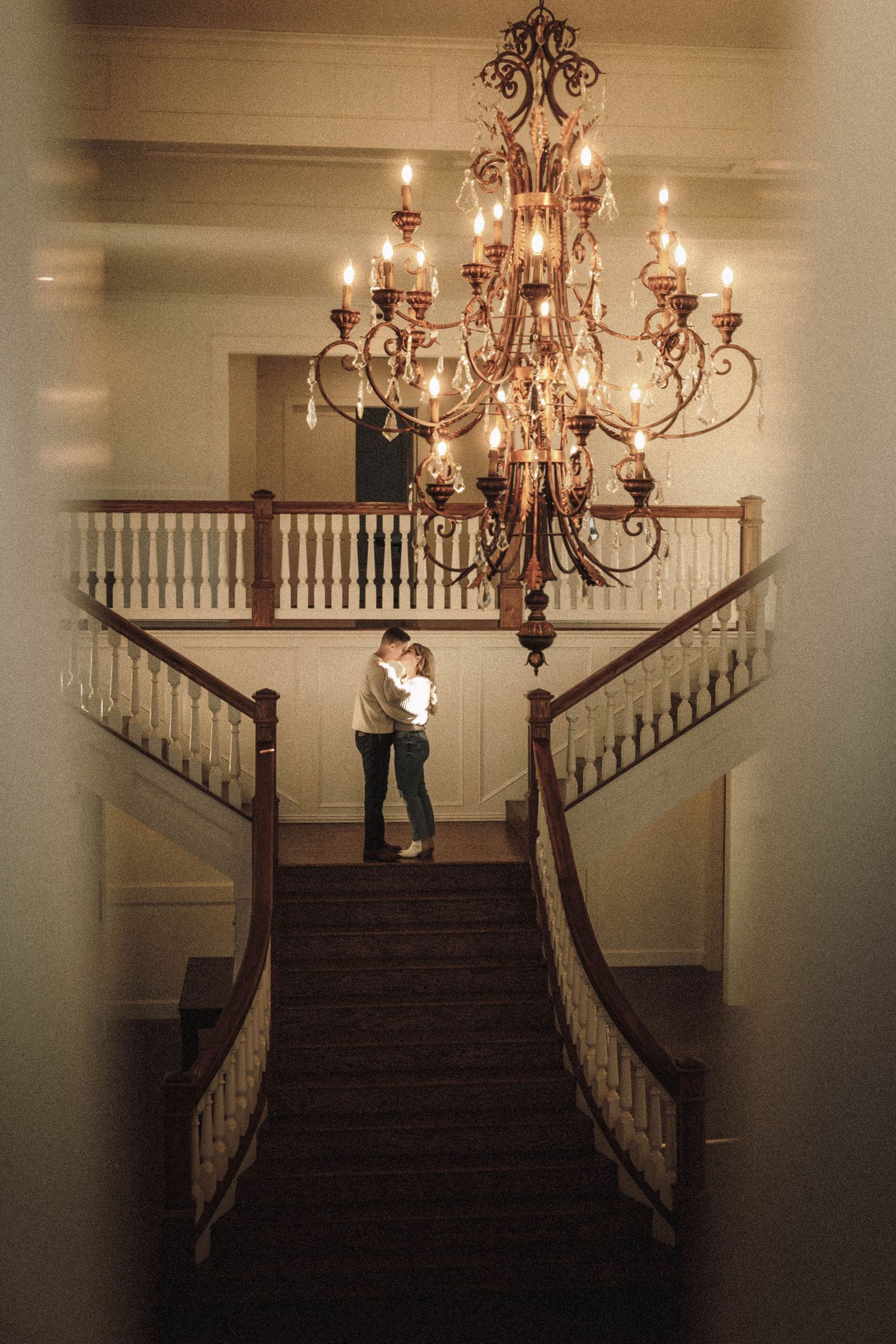 Elegant grand staircase with chandelier creates dramatic silhouettes in warm lighting.