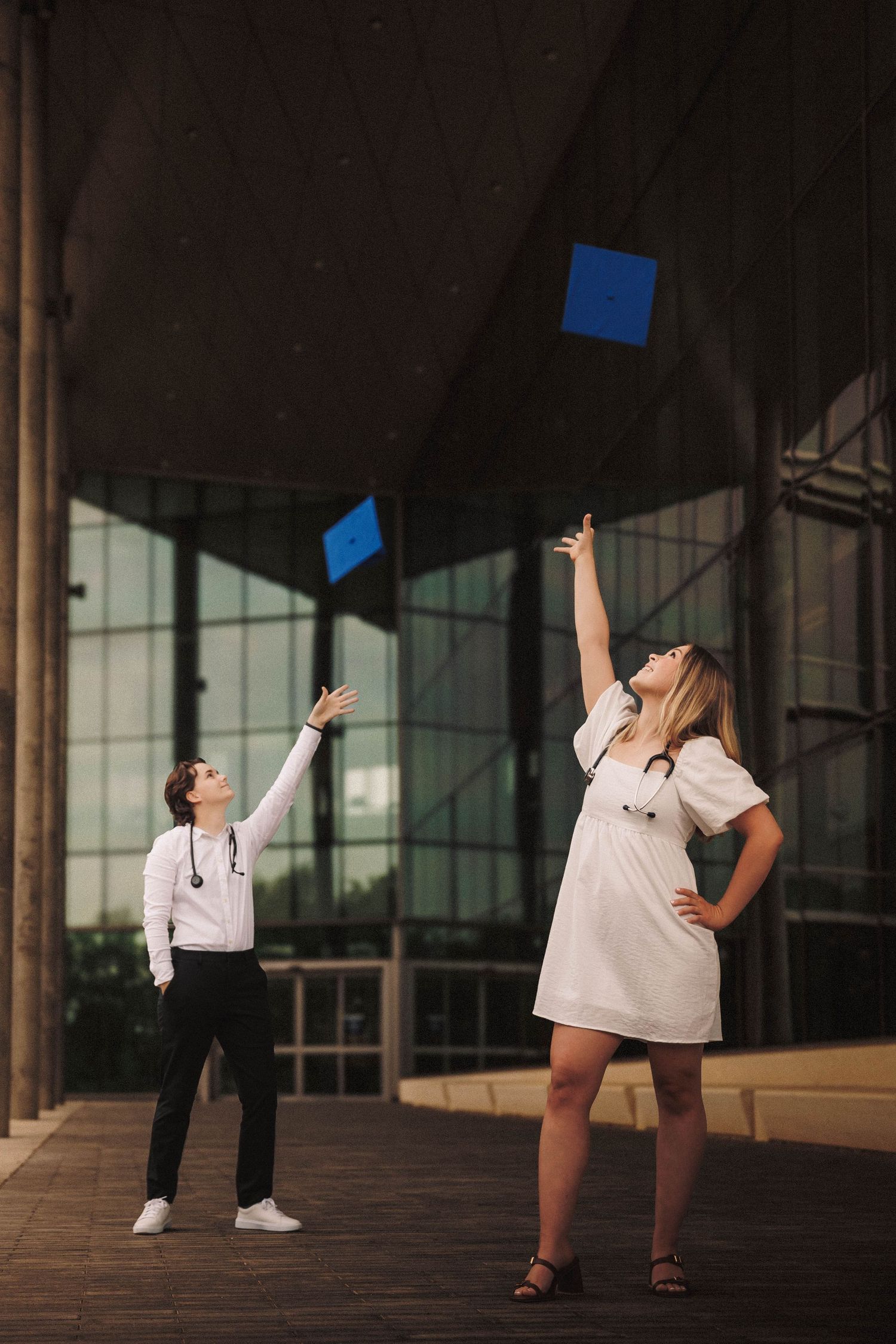 Graduates tossing blue caps in celebration outside modern building with pillars.