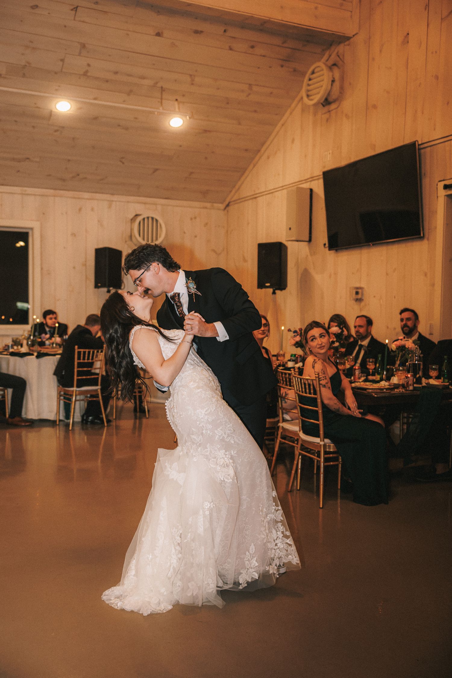 Bride and groom share first dance dip kiss in rustic wood reception hall.