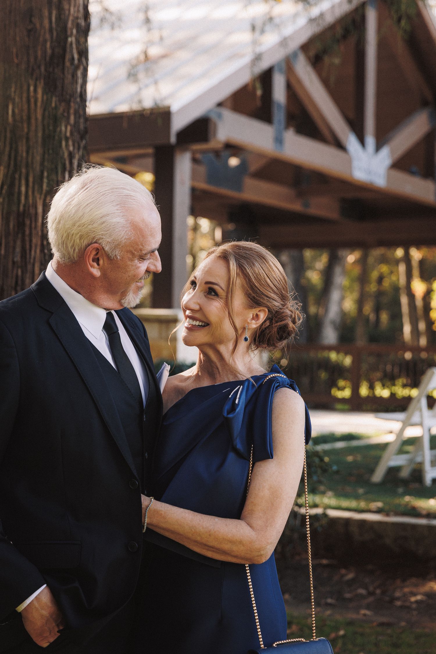 Elegant older couple in formal attire sharing a tender moment outdoors at a wedding venue.