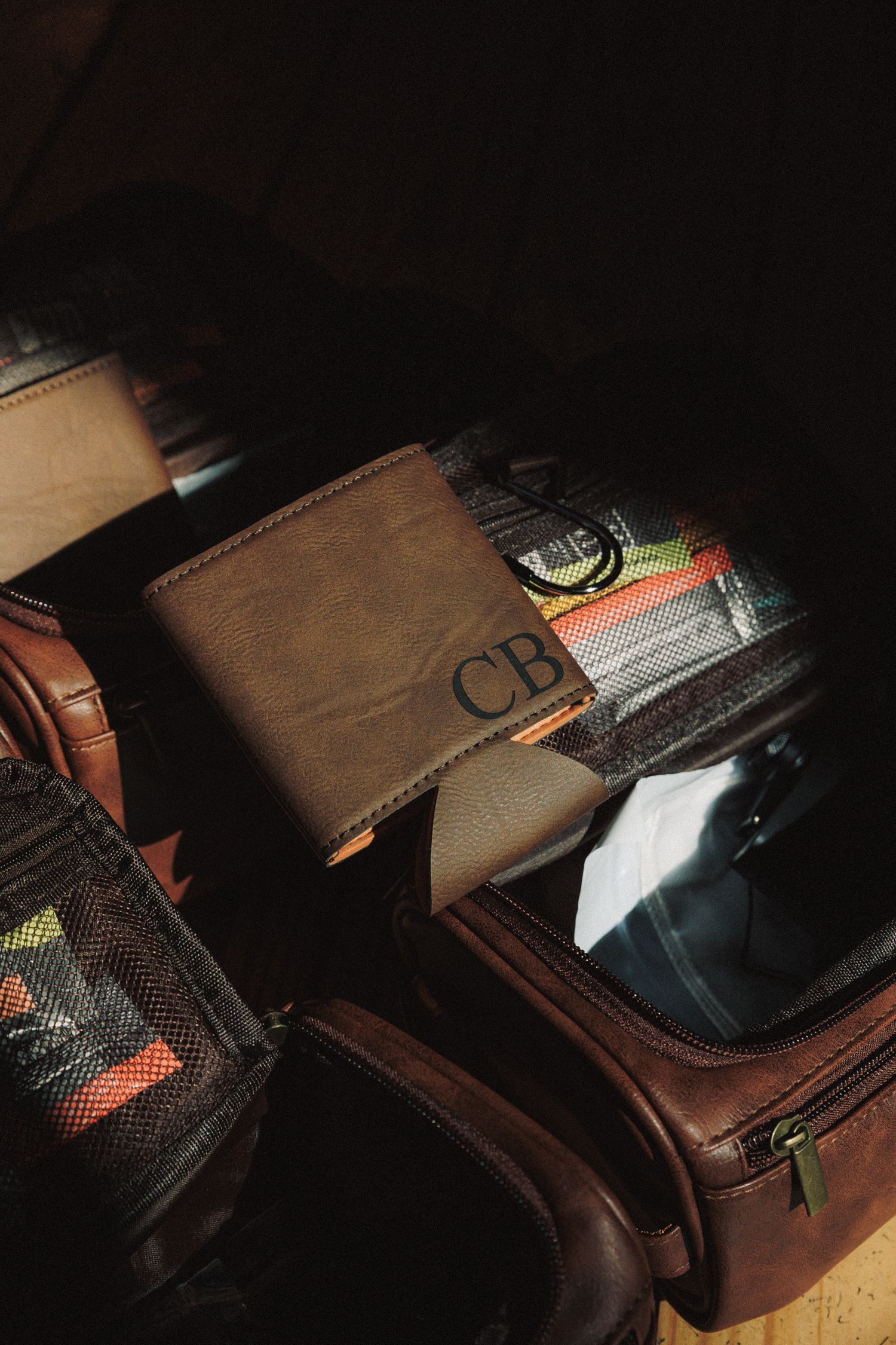 Monogrammed leather wallet gift with initials CB displayed among groomsmen accessories in dark lighting.