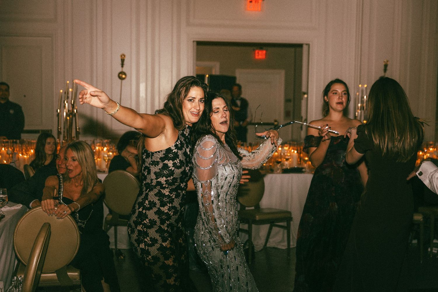 Women in elegant gowns dancing energetically at glamorous candlelit wedding reception celebration.