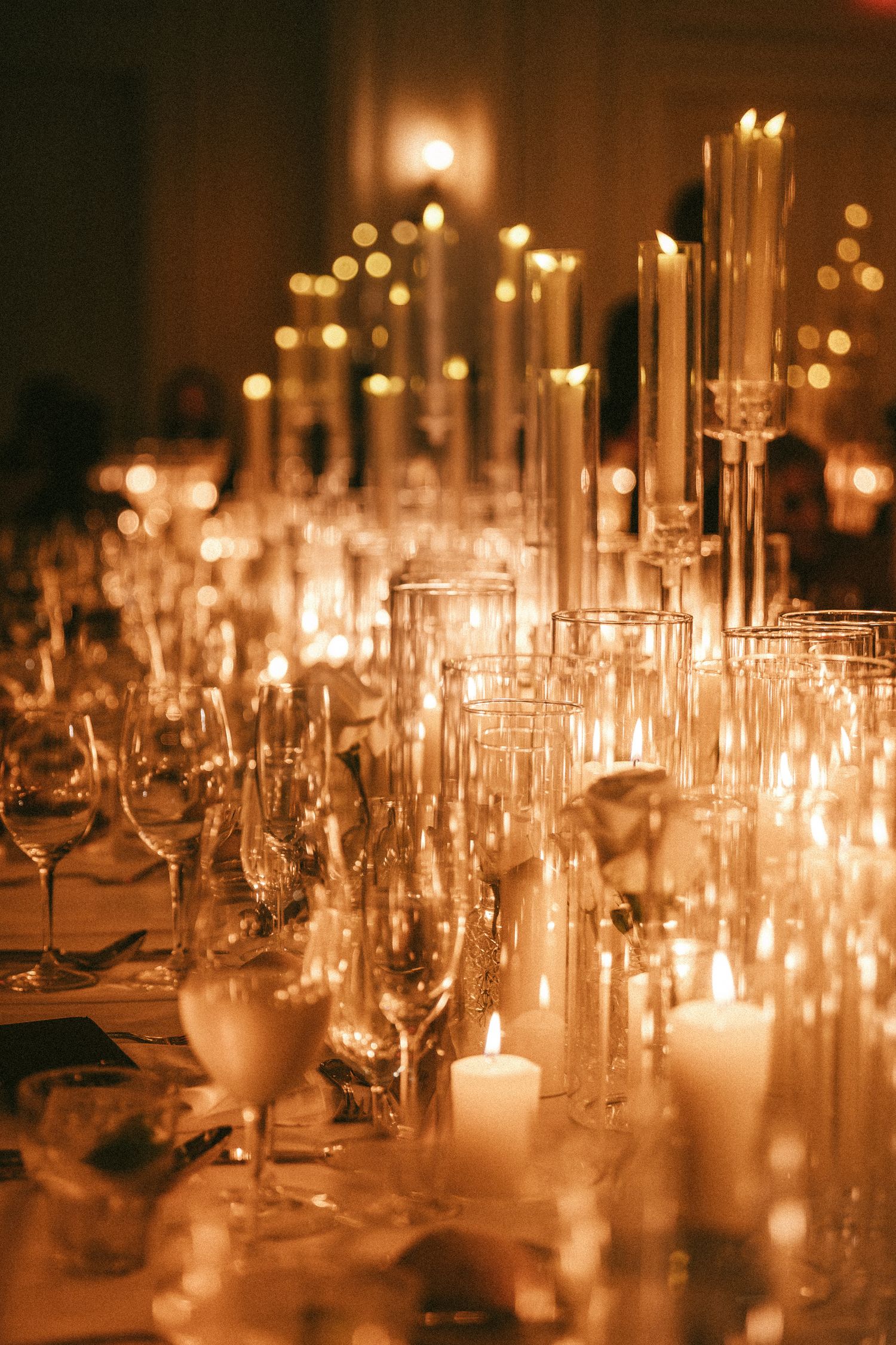 Romantic wedding reception tablescape with tall taper candles and crystal glassware in warm light.