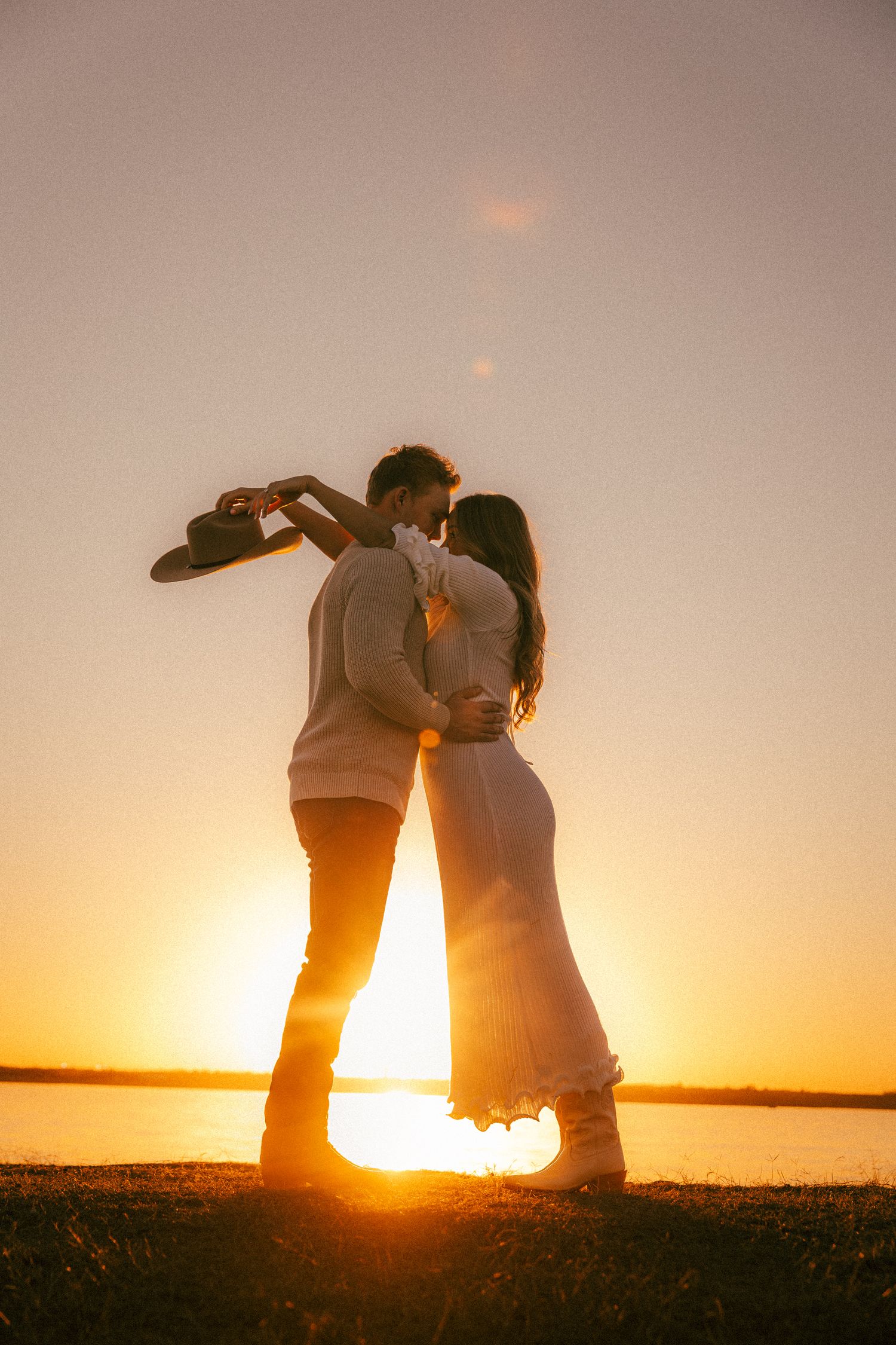 Silhouettes of a couple embracing against a dramatic sunset over water.