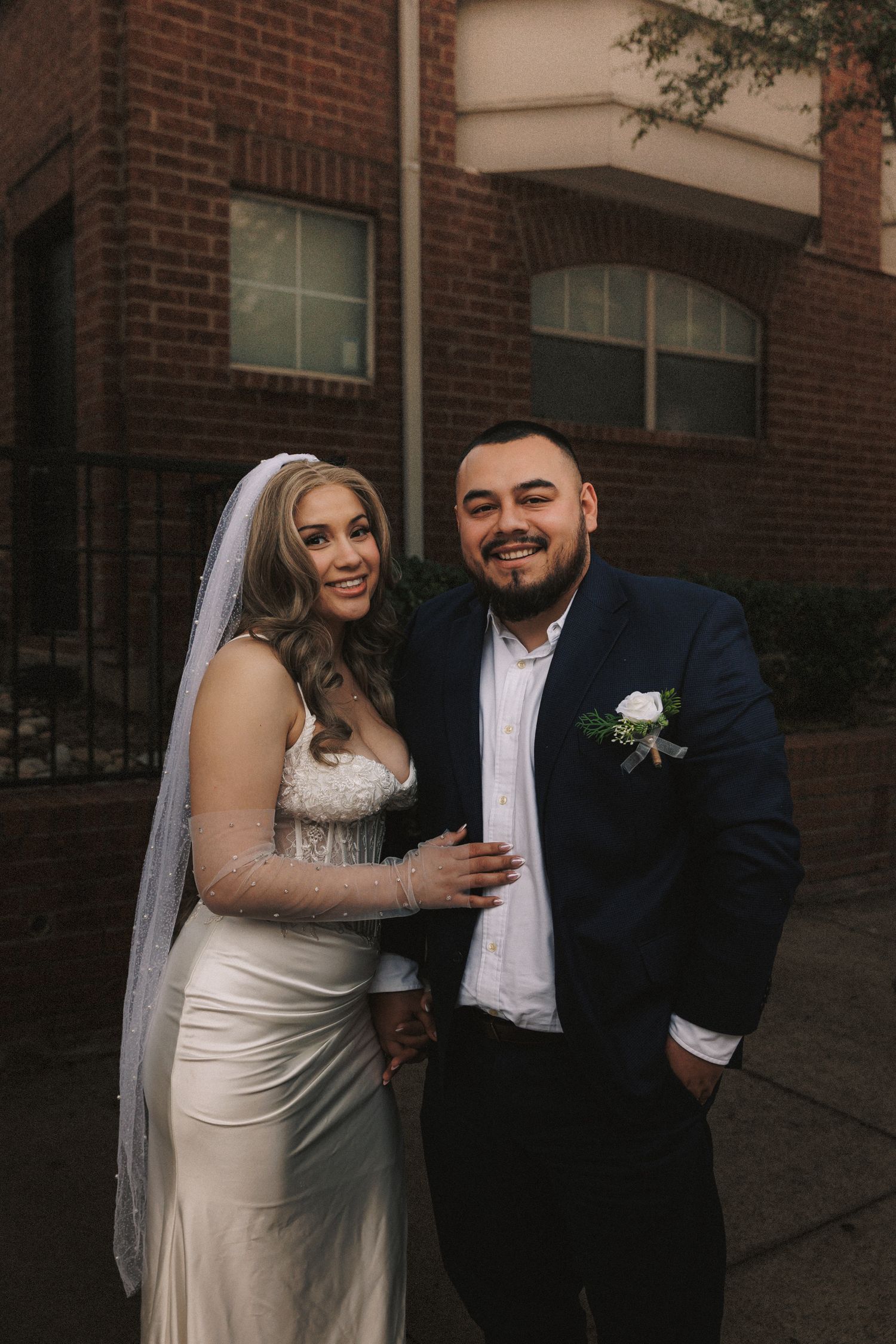 A wedding couple shares joyful moments against a brick building backdrop.