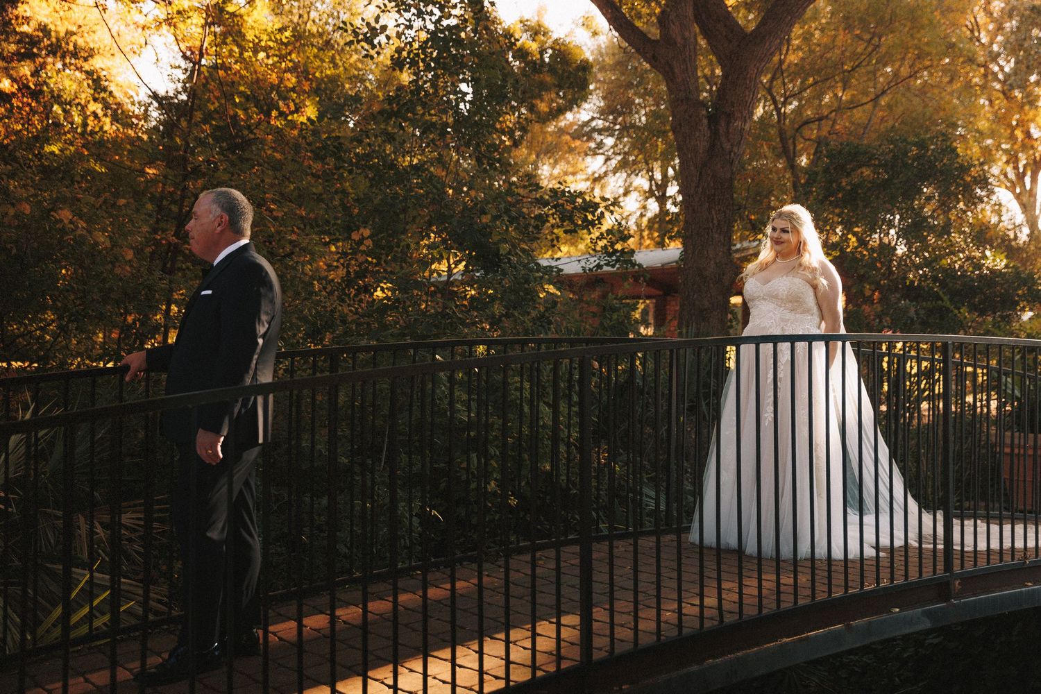 Bride in ball gown surprises man on garden bridge during romantic first look at sunset.