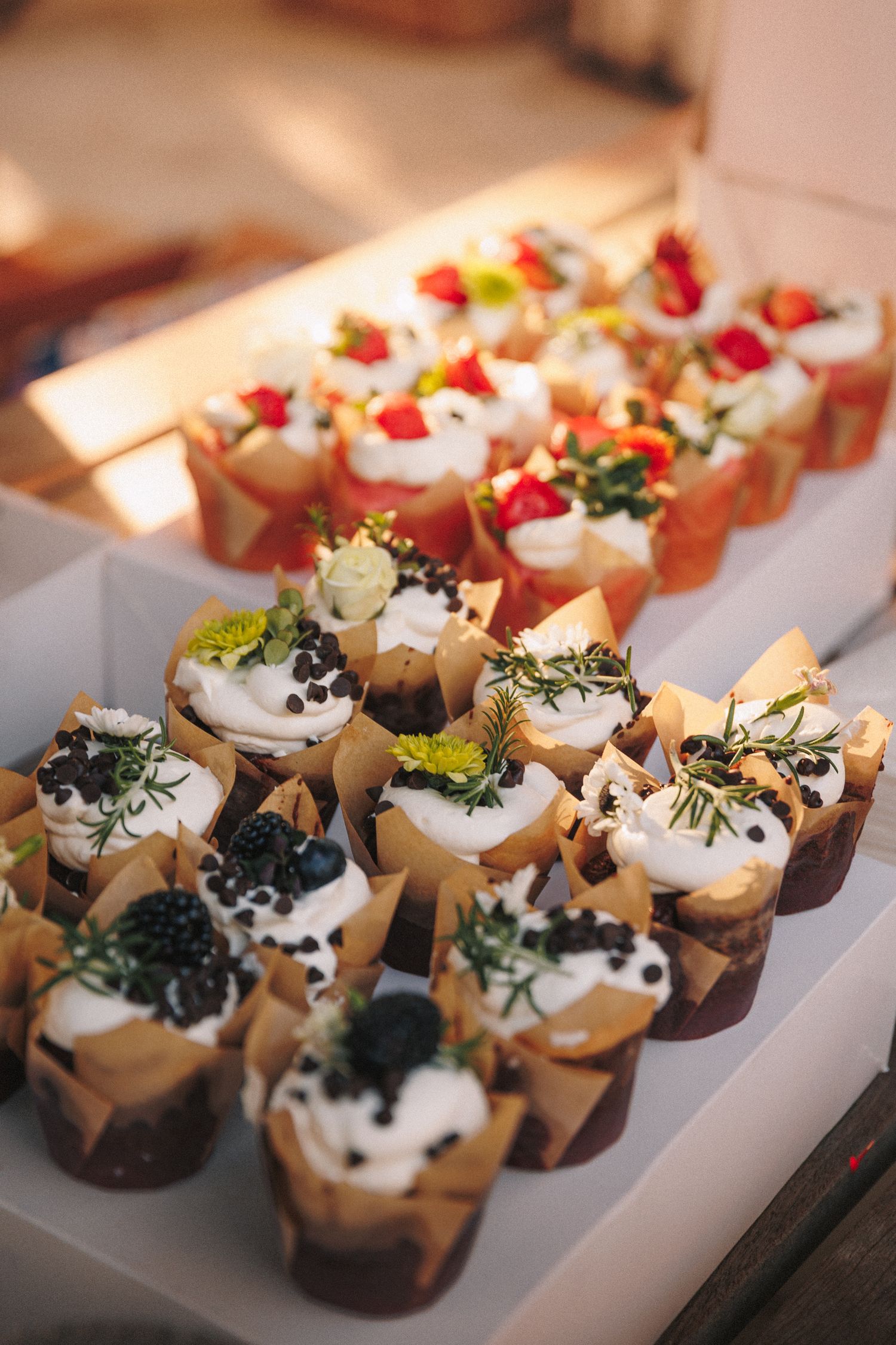 Elegant assorted cupcakes topped with whipped cream, fresh berries, caviar, and herbs displayed on a white tray.