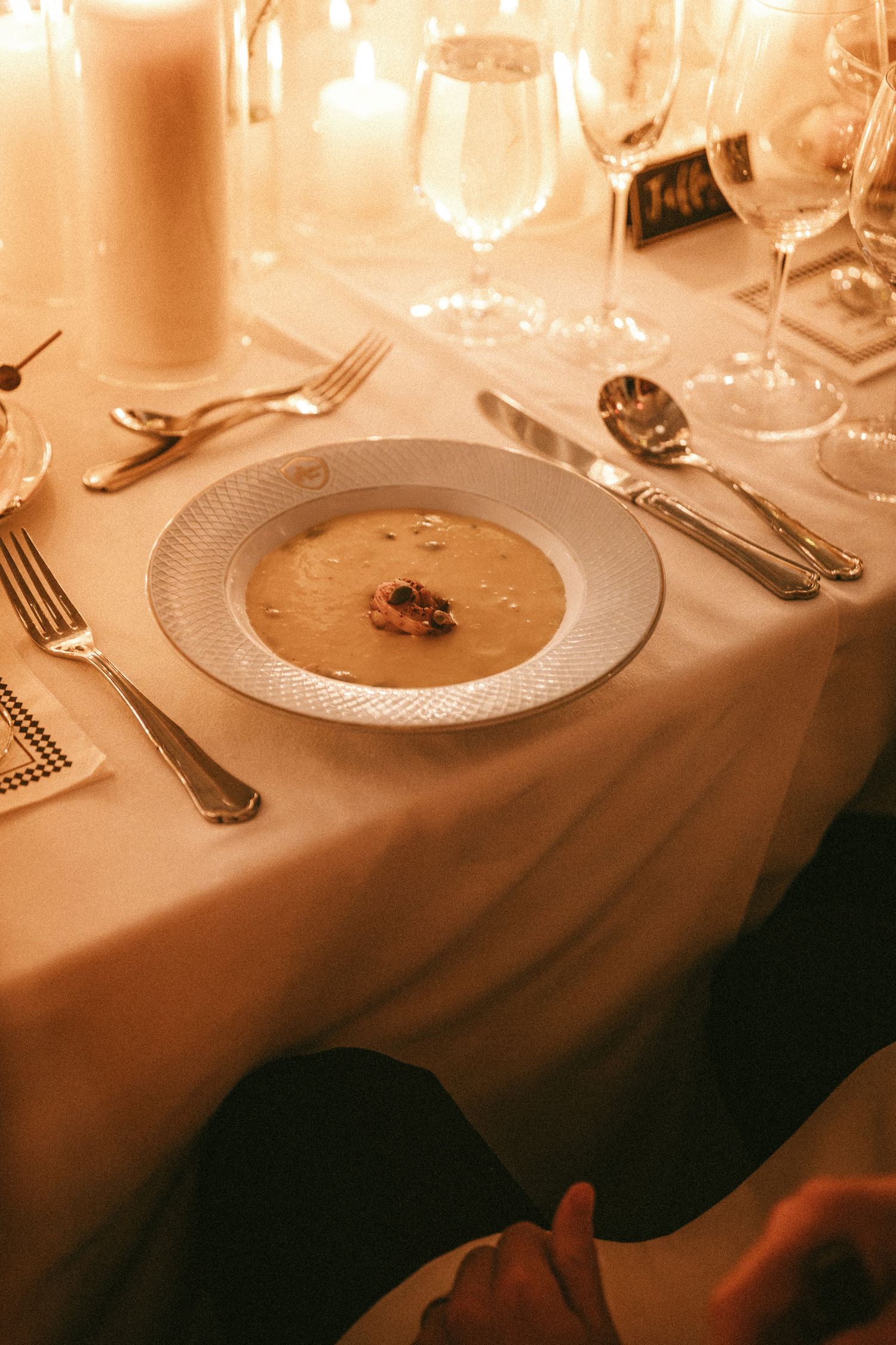 An elegant wedding reception place setting with soup course, candles, and crystal glassware.
