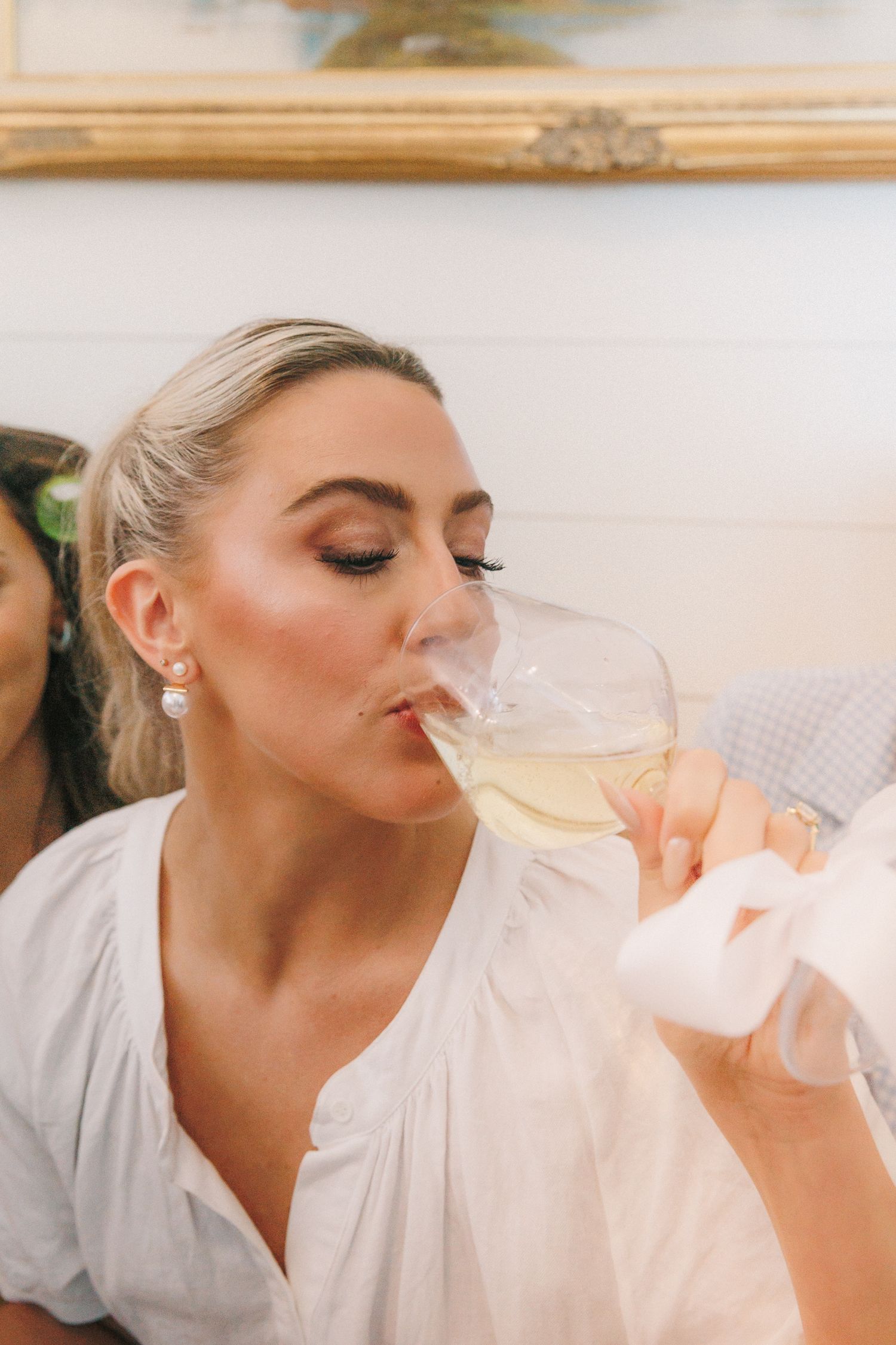 Person in white robe sipping champagne during wedding morning preparations.