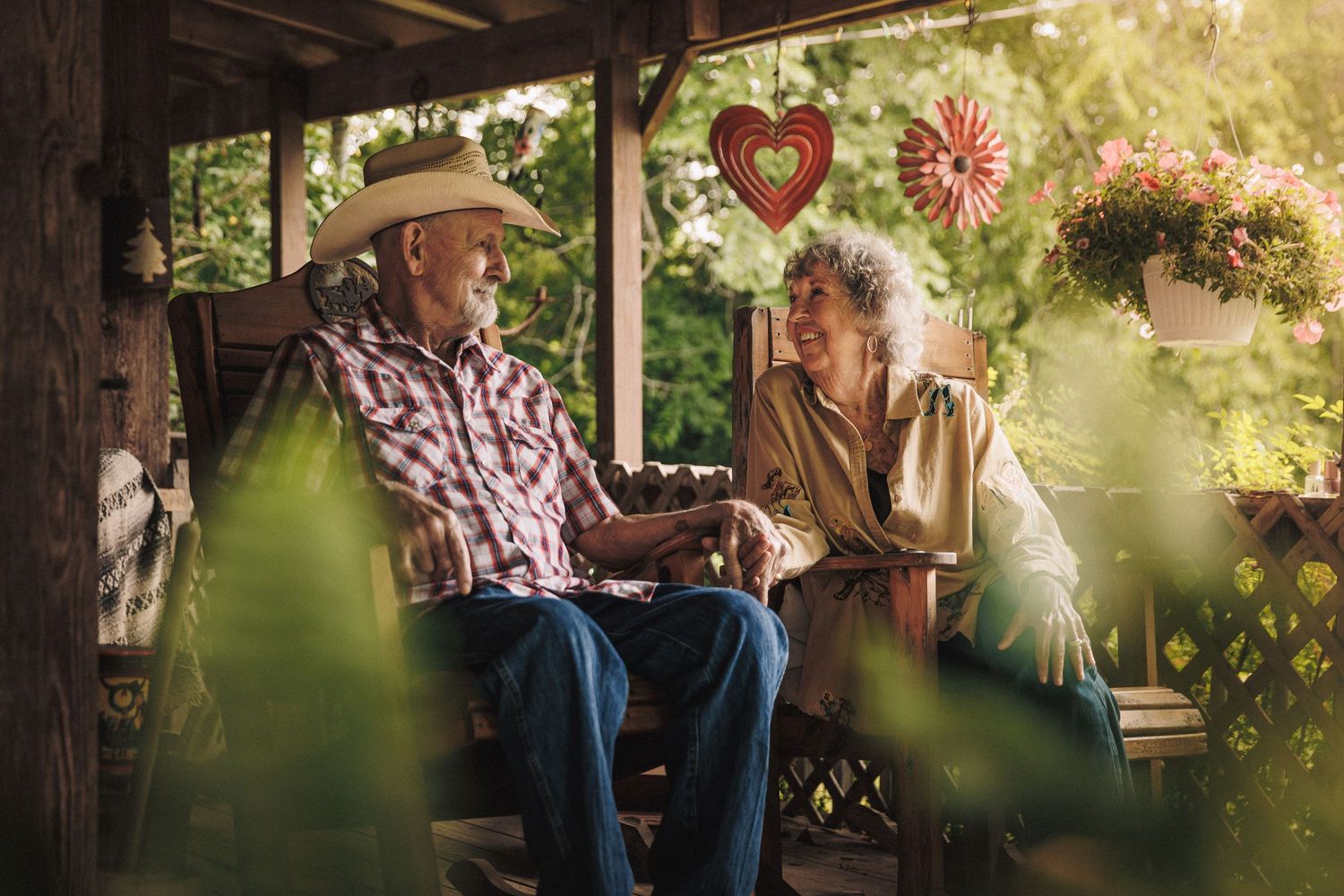 Senior couple enjoying conversation while sitting on a porch bench during a sunny afternoon.
