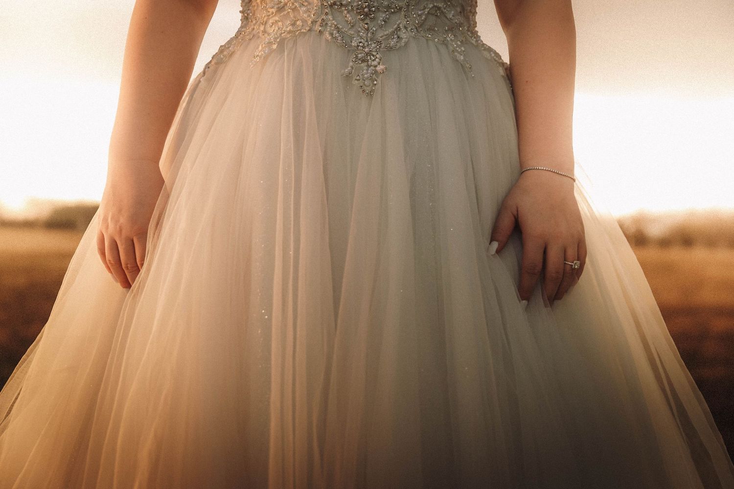 Wedding dress details showing cascading layers of white tulle fabric in warm sunlit setting.