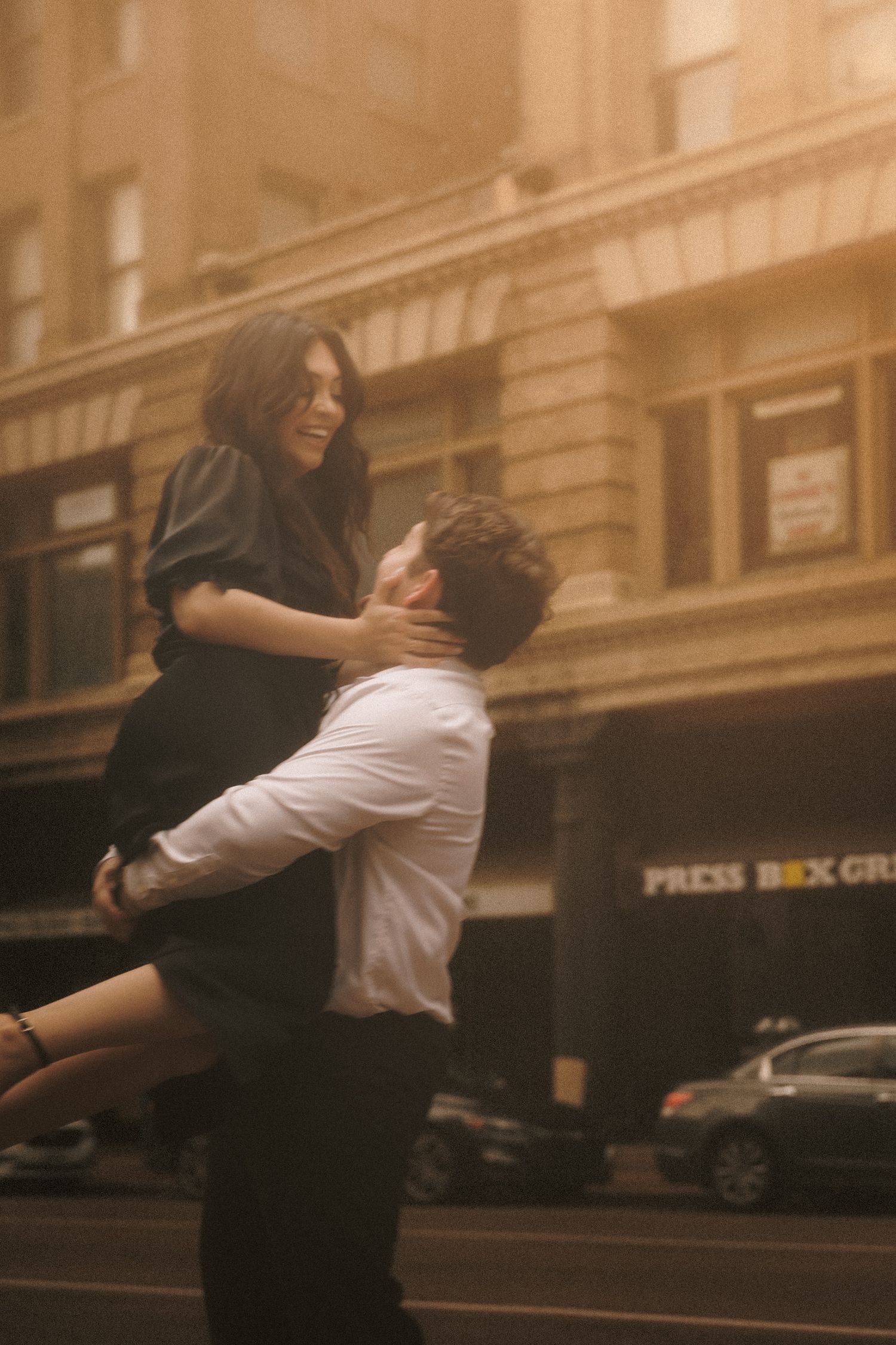 A joyful couple embracing on a city street, man lifting woman in a romantic golden-hued urban setting.