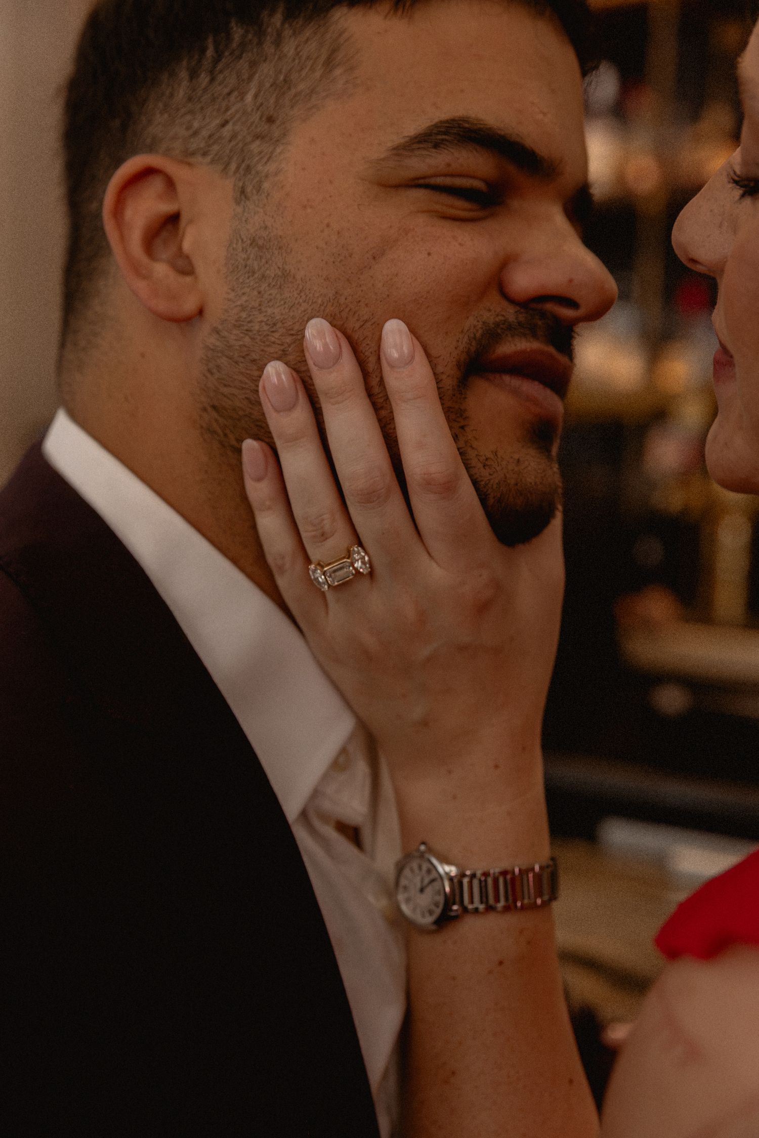 Man smiling as woman with engagement ring and watch gently touches his face.