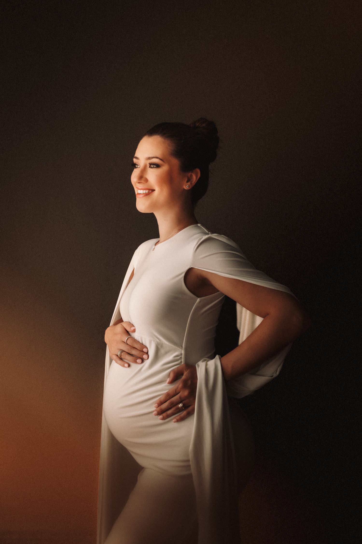 A series of maternity photos showing a pregnant belly in white dress against a dark background with dramatic lighting.