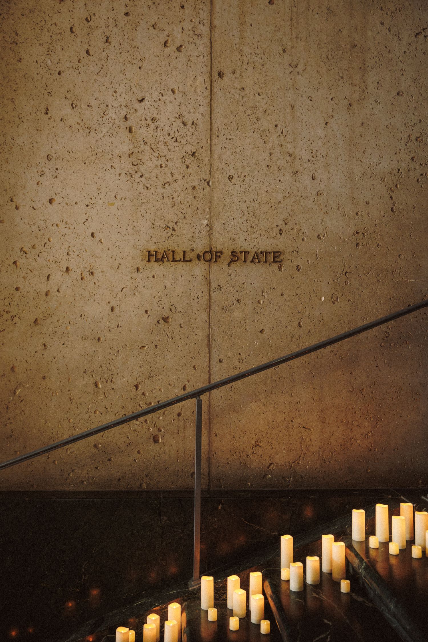 Hall of State building wall with gold lettering and rows of glowing white candles on dark marble steps.