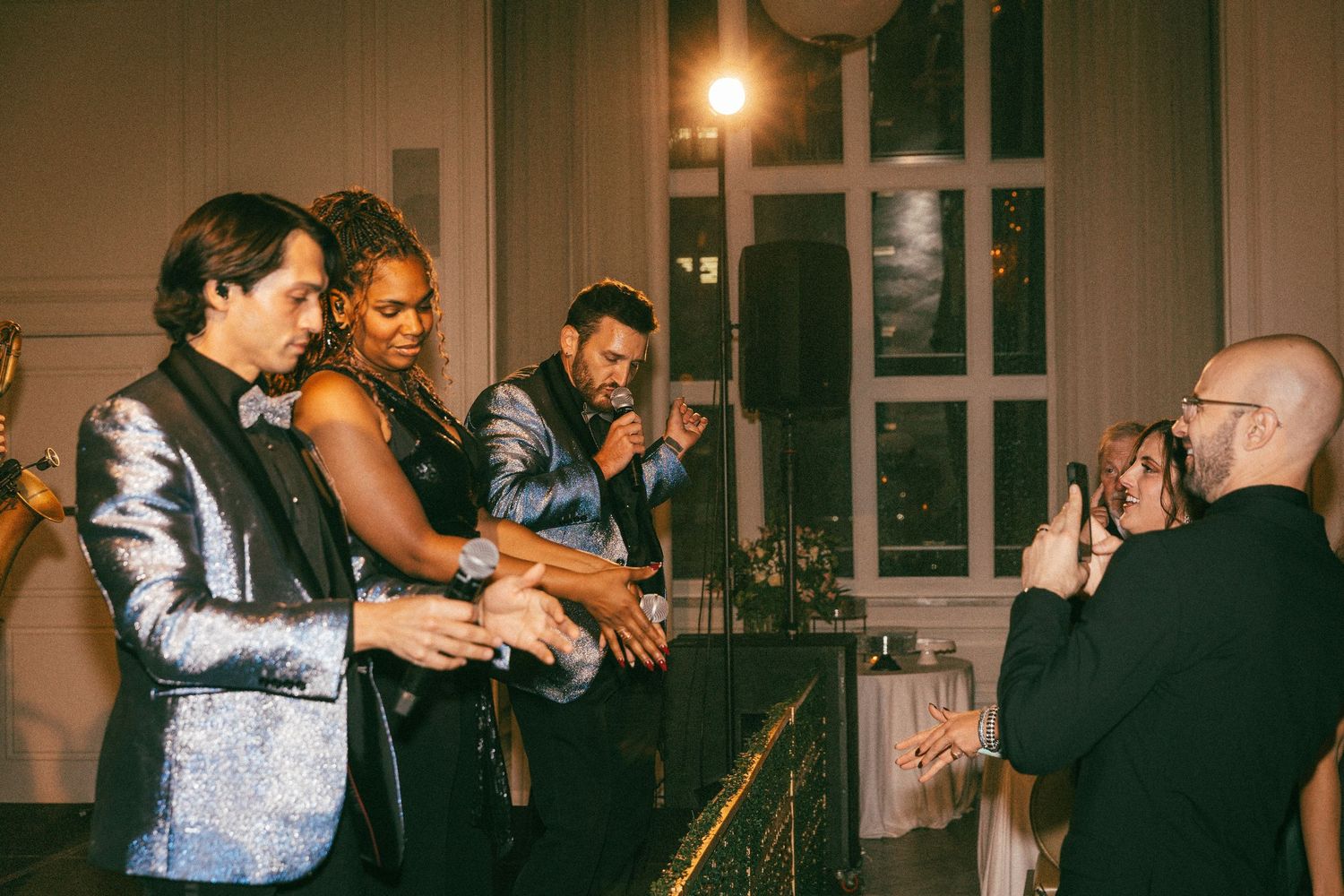 Wedding guests celebrating at bar with woman in elegant dress and men in formal attire.