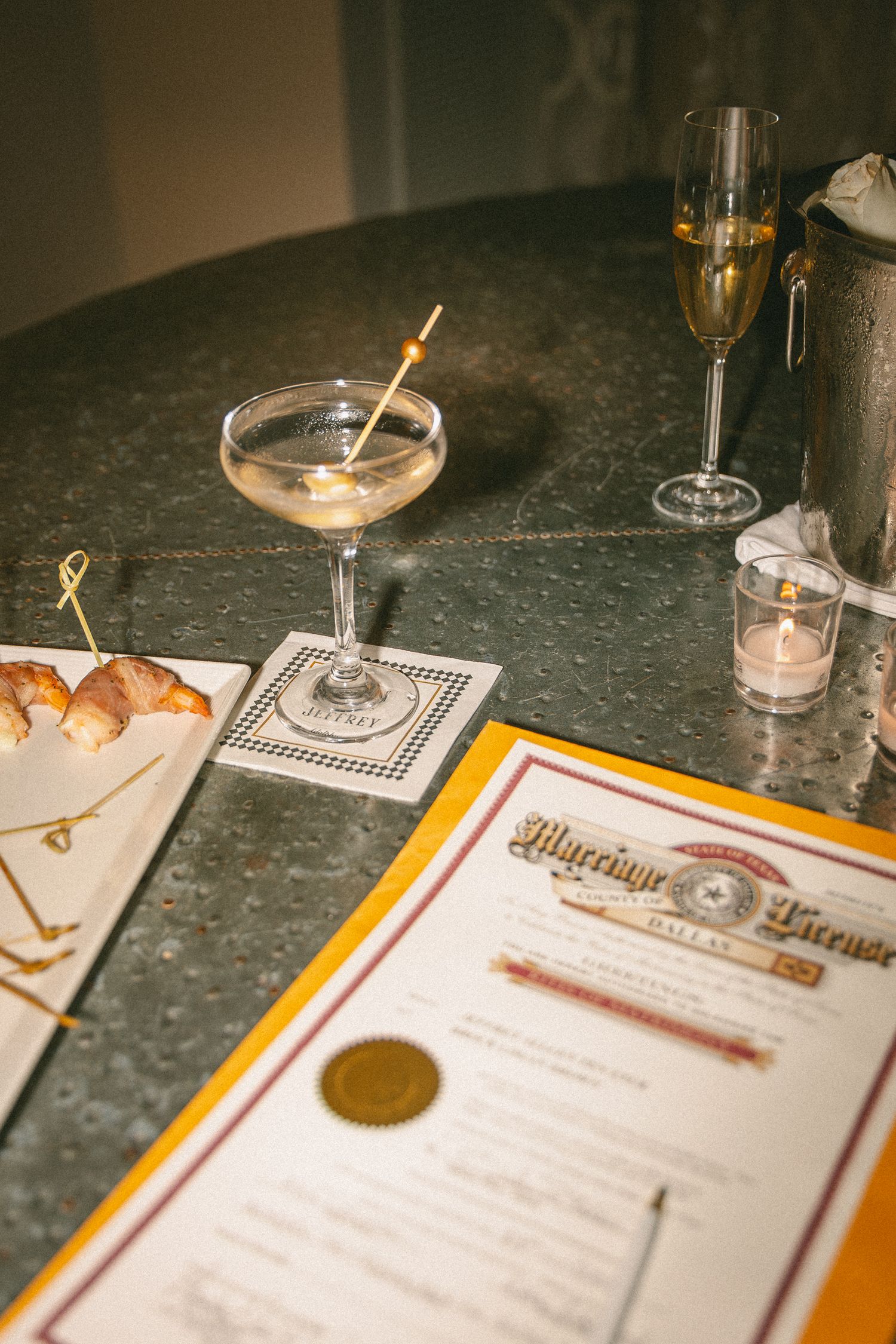 Wedding marriage license displayed beside a martini cocktail and champagne glass at a reception.
