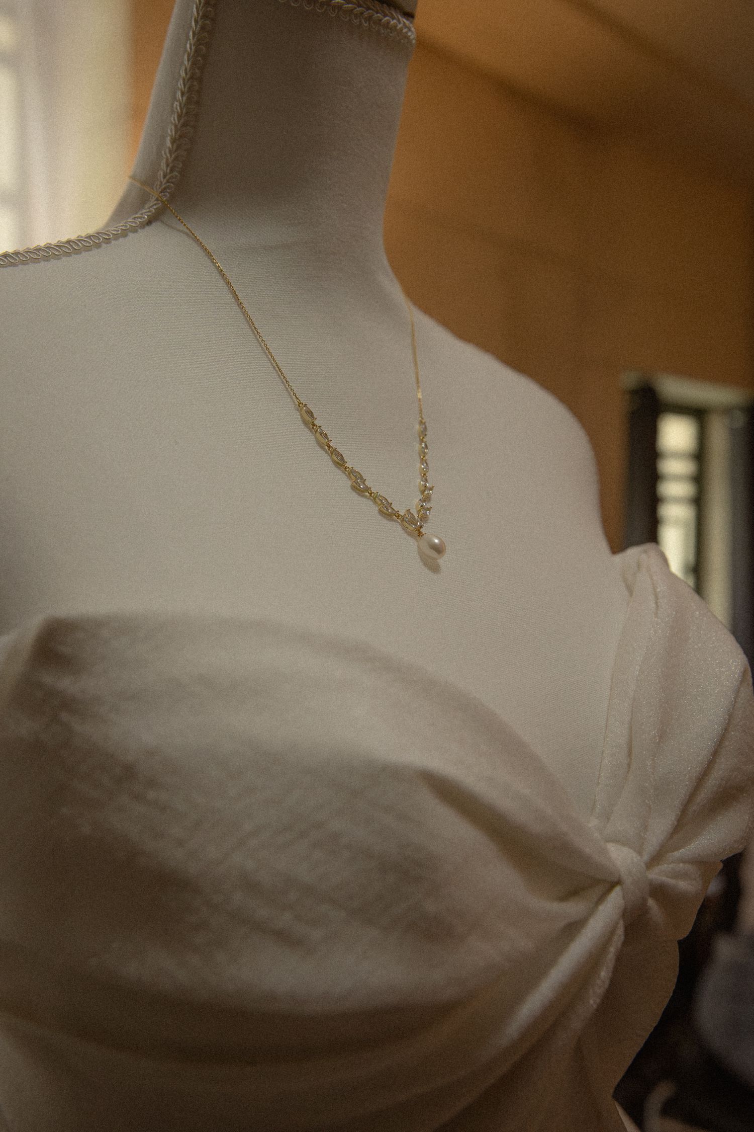 Gold chain necklace with pearl pendant displayed on a white wedding dress mannequin.