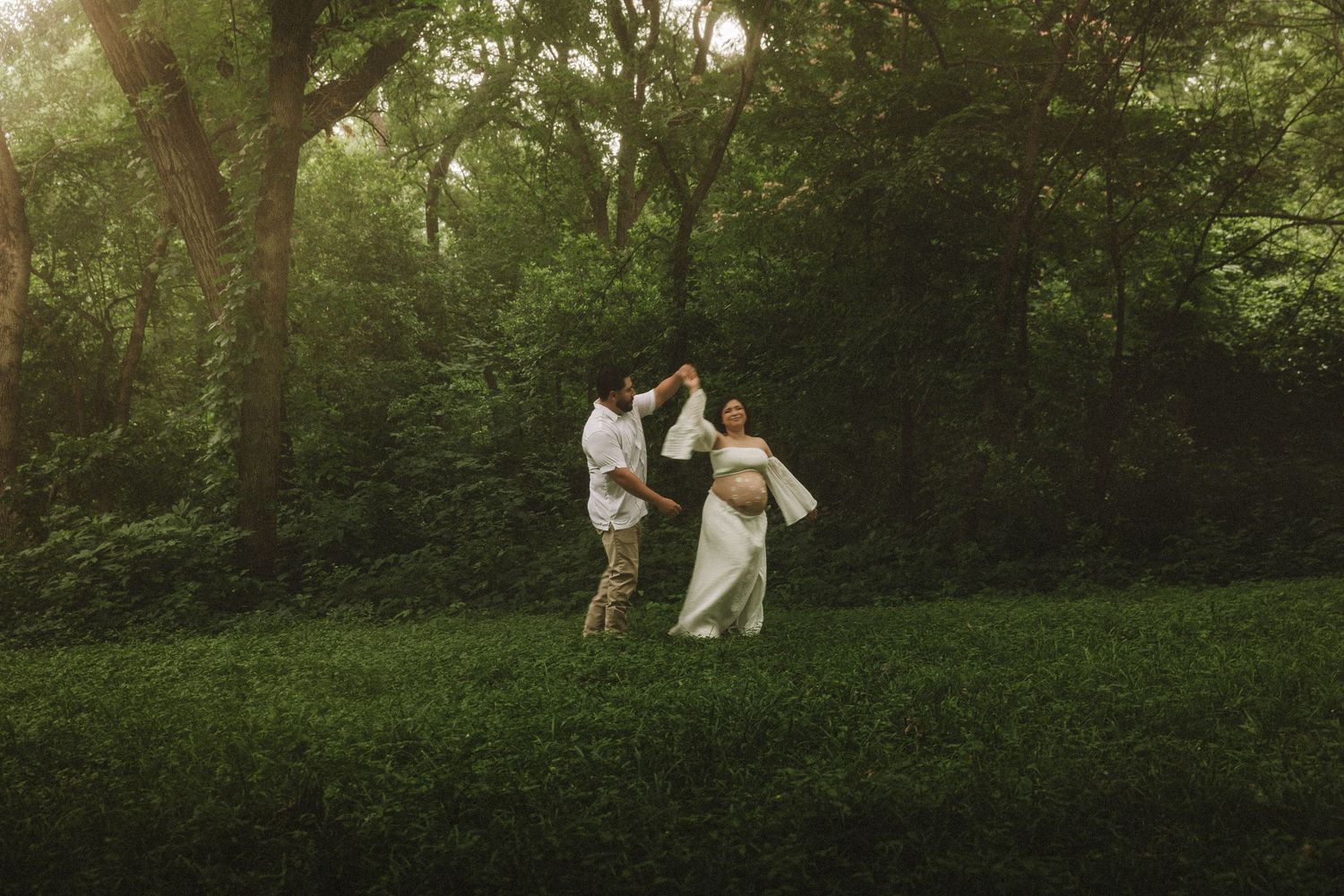 A couple walks together through a lush green forest path on a sunny day.