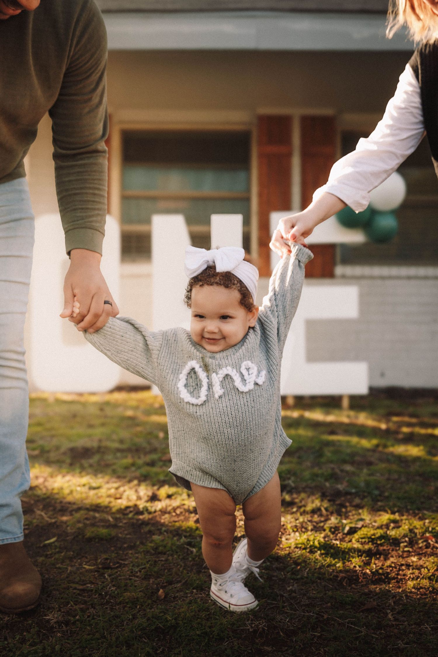 A series of photos showing an infant in a gray romper being supported while practicing walking on grass at sunset.
