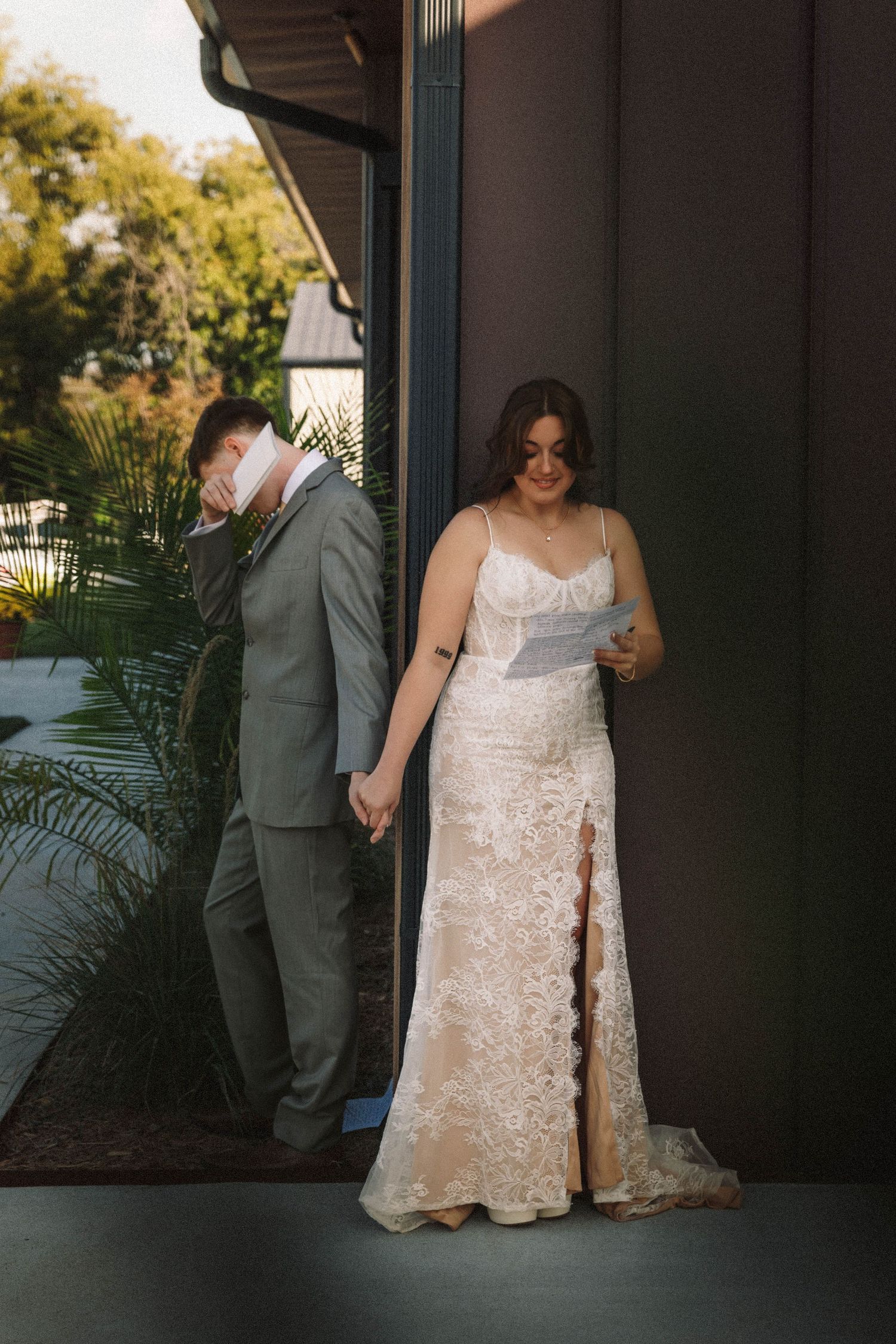 A couple shares an intimate moment during their wedding photoshoot at an outdoor venue with palm trees and greenery.
