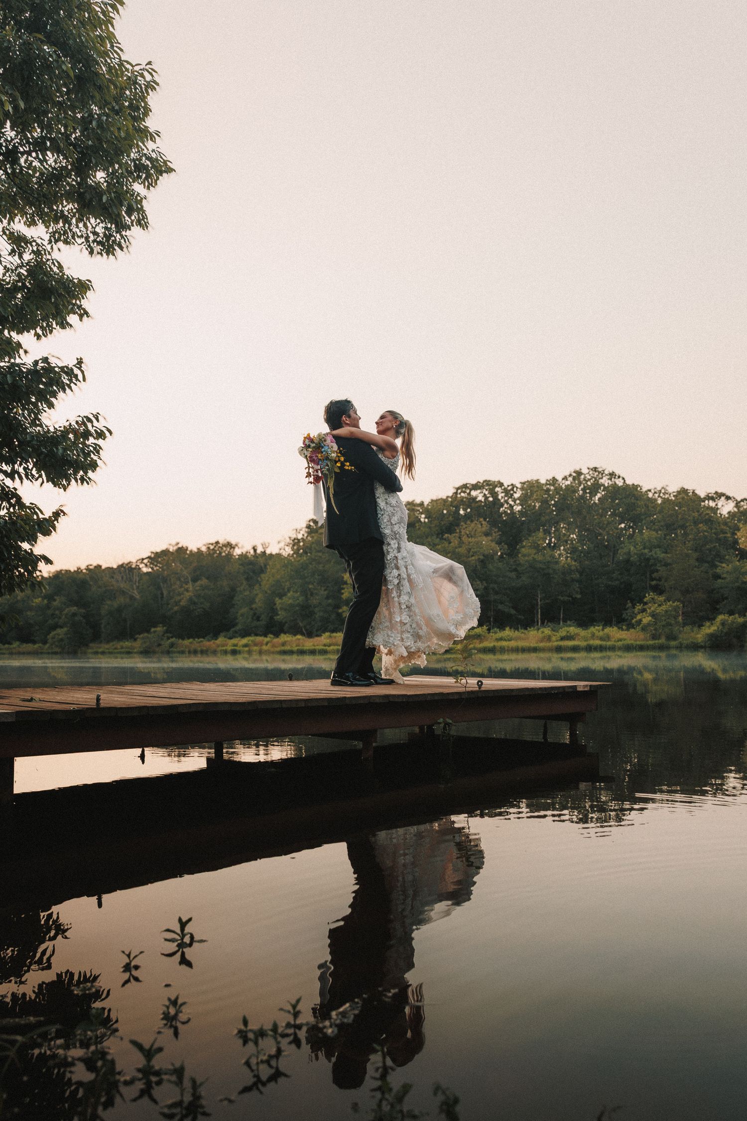 A couple shares a romantic moment on a wooden dock overlooking a serene lake at sunset.