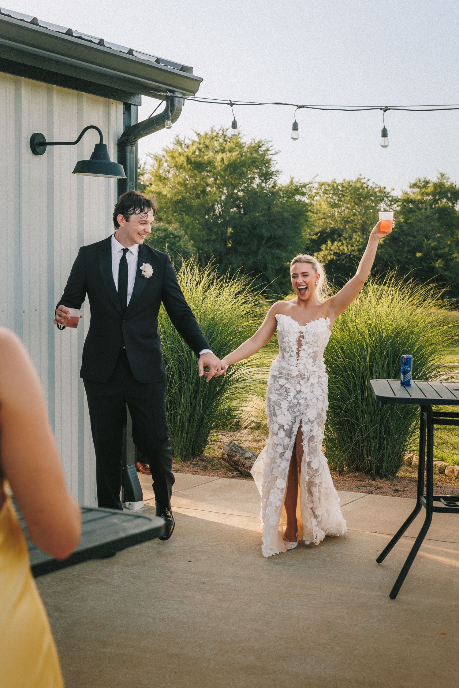 Wedding party dancing and celebrating on outdoor patio near white building.