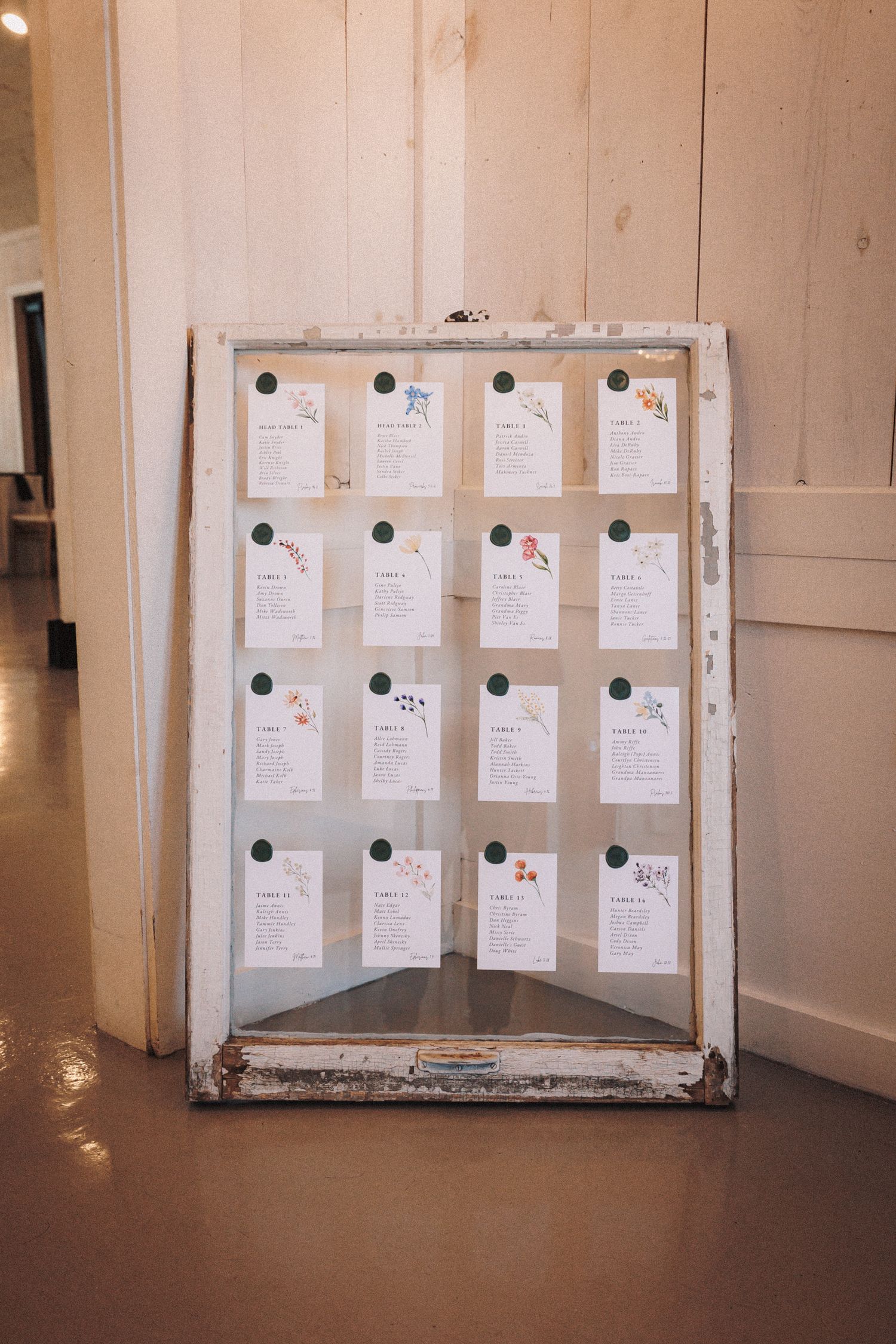 Rustic white vintage window frame used as a wedding seating chart display with floral cards.