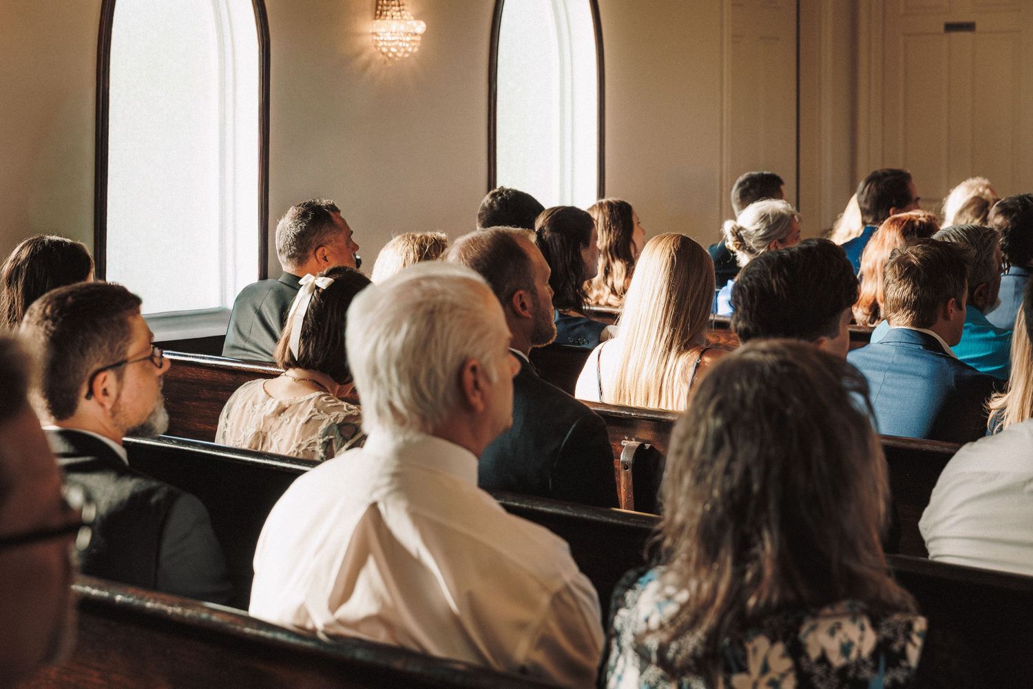 Wedding guests seated in church pews during an intimate ceremony in a bright chapel.